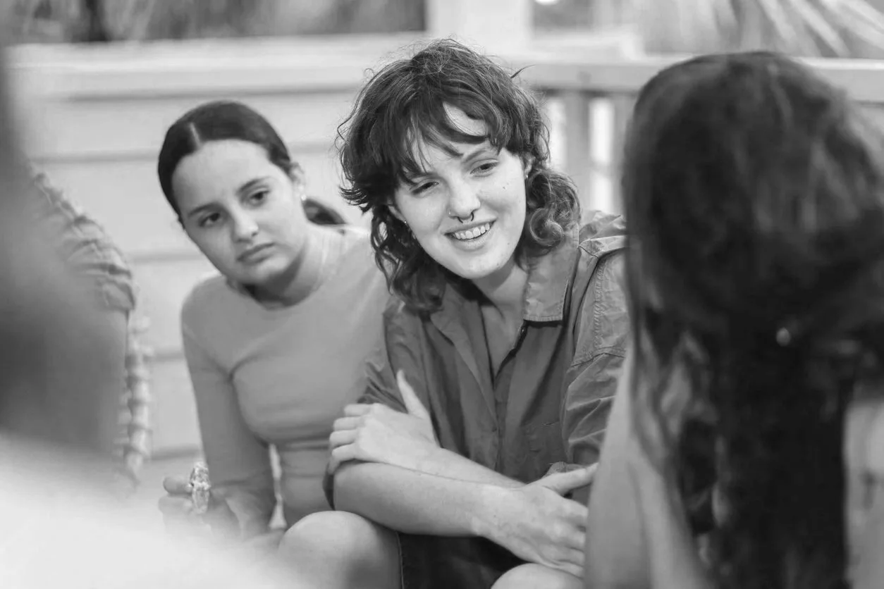 Four young women sitting together, engaged in conversation, outdoors.
