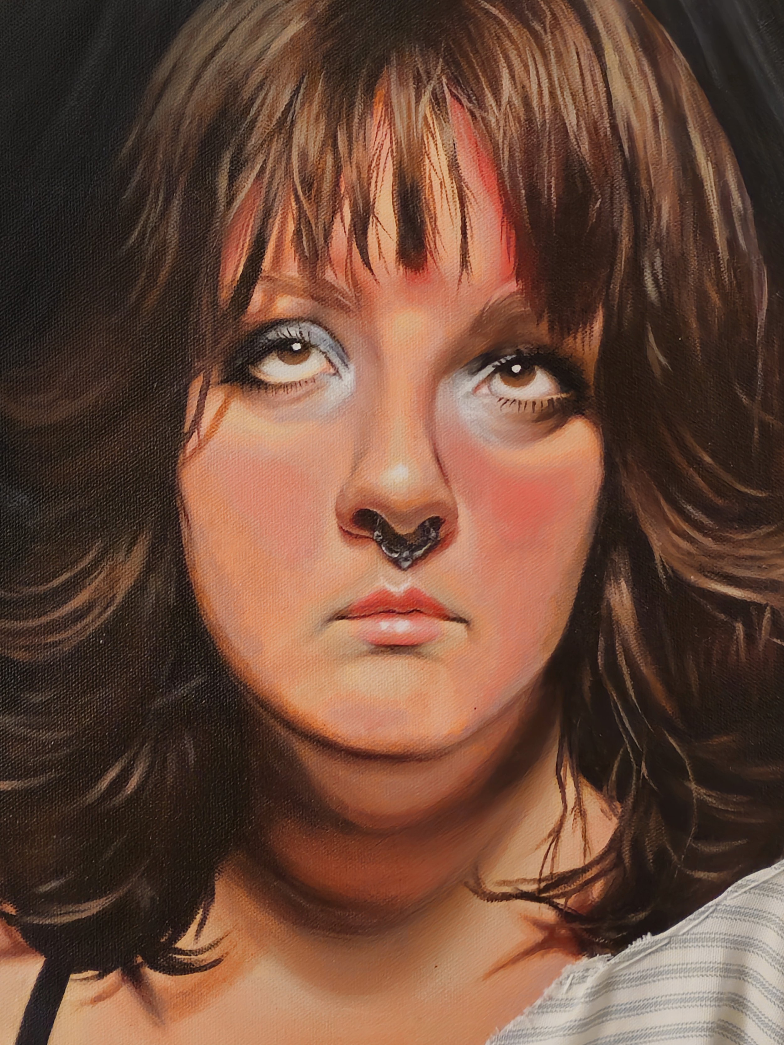 A portrait of a woman with dark hair, makeup, and a silver nose ring, looking up into a light.