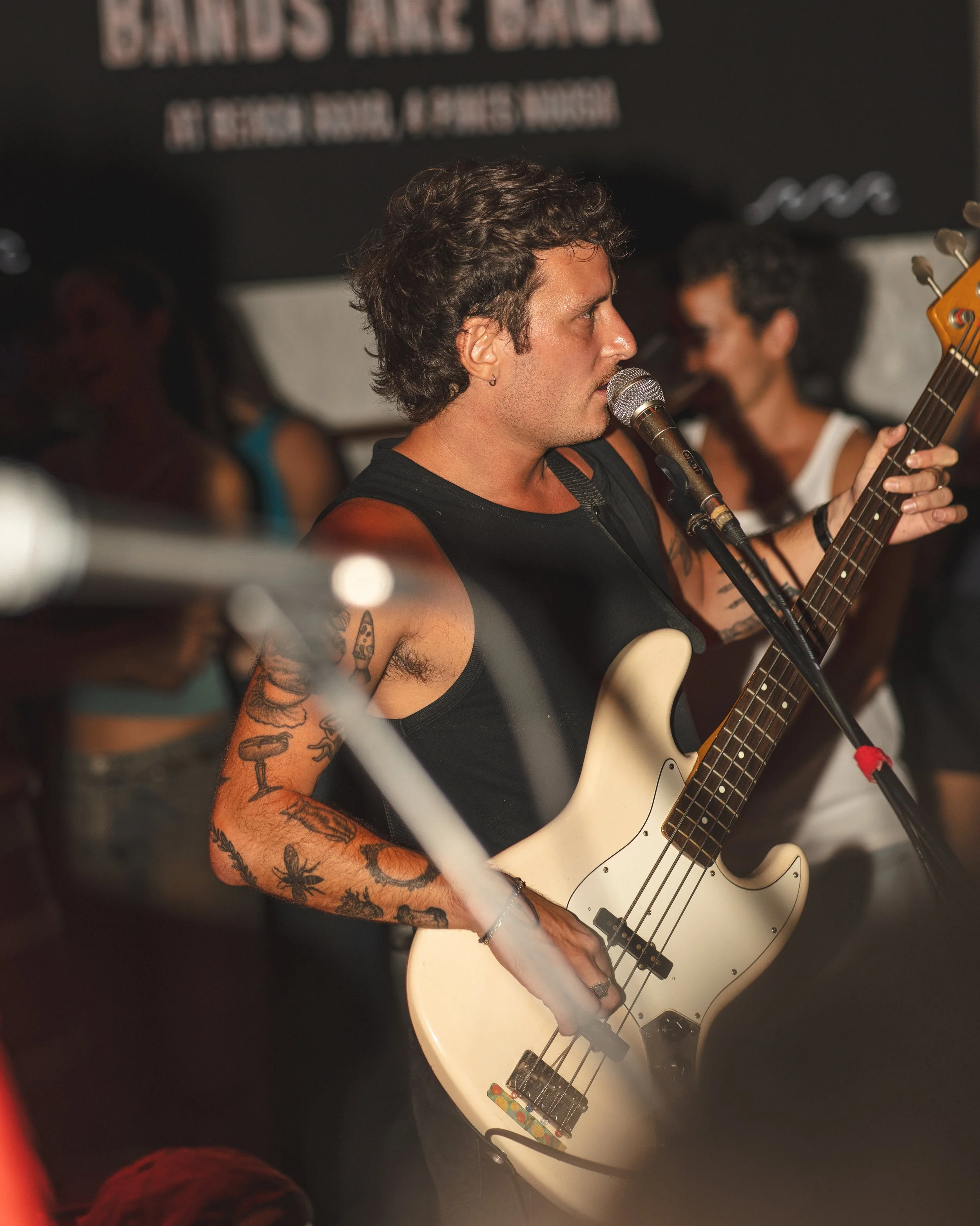 Live music performance in Noosa featuring a male bass guitarist singing on stage, with audience and bar setting in the background – Sunshine Coast event and nightlife photography