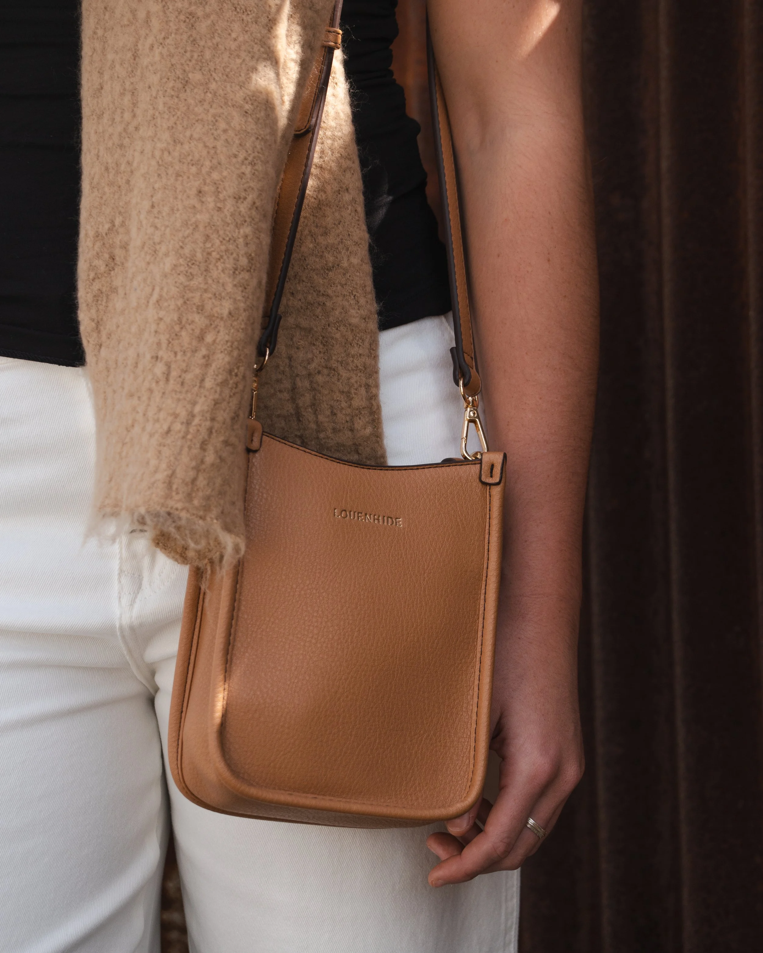 Person wearing a beige fuzzy sweater, black top, and white pants, carrying a tan crossbody bag with gold hardware and the brand name 'LOUENHIDE' on it.