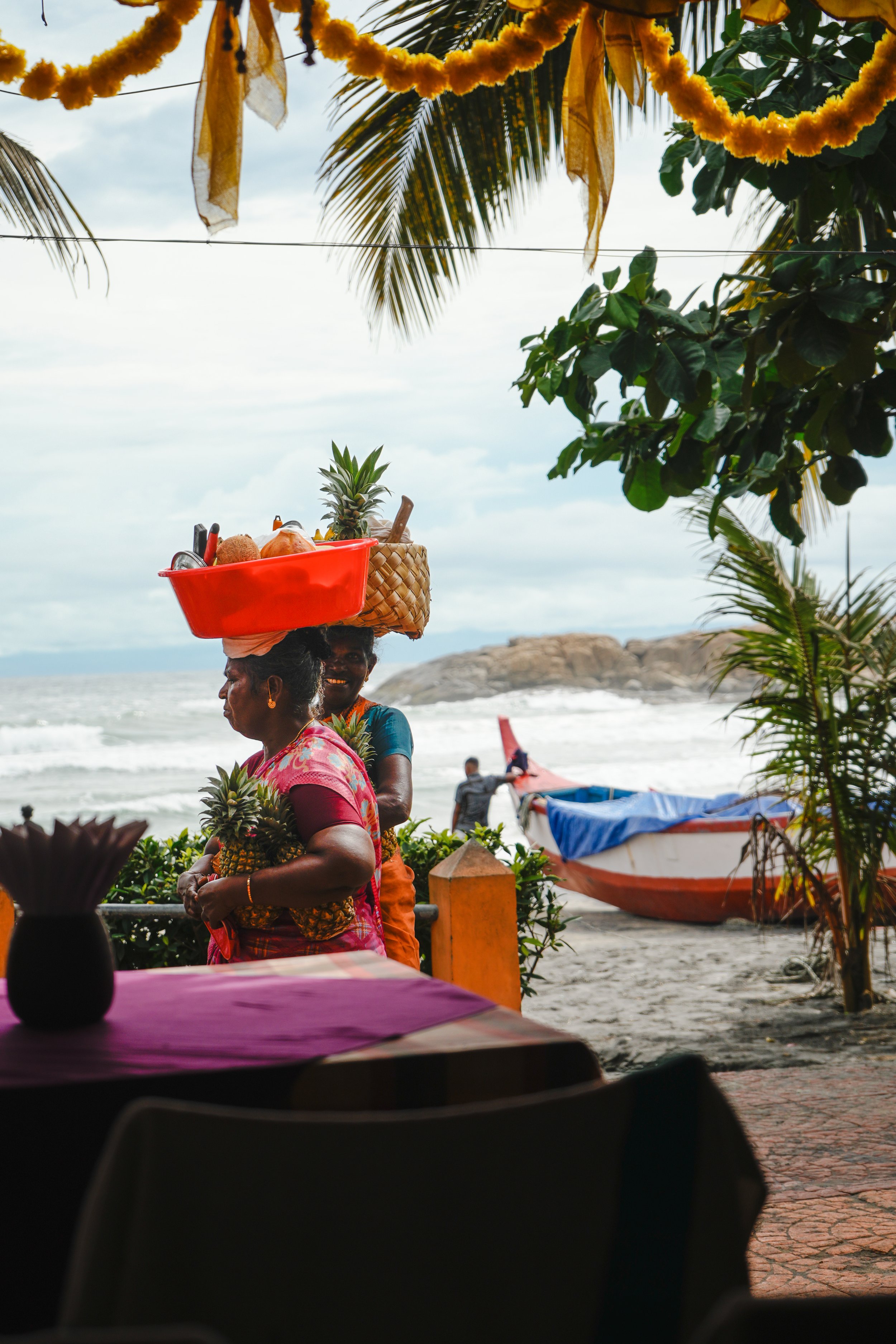 Travel photography of fruit vendors carrying pineapples along an Indian beach shoreline