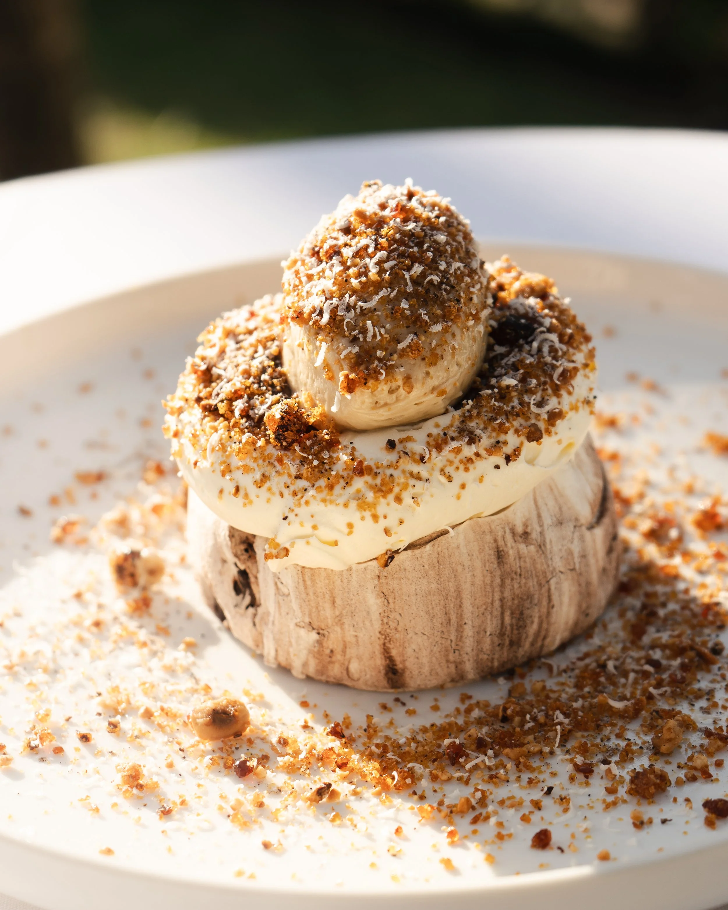 A dessert with a mushroom-shaped top, ice cream, whipped cream, and crumbled cookies or nuts on a white plate.