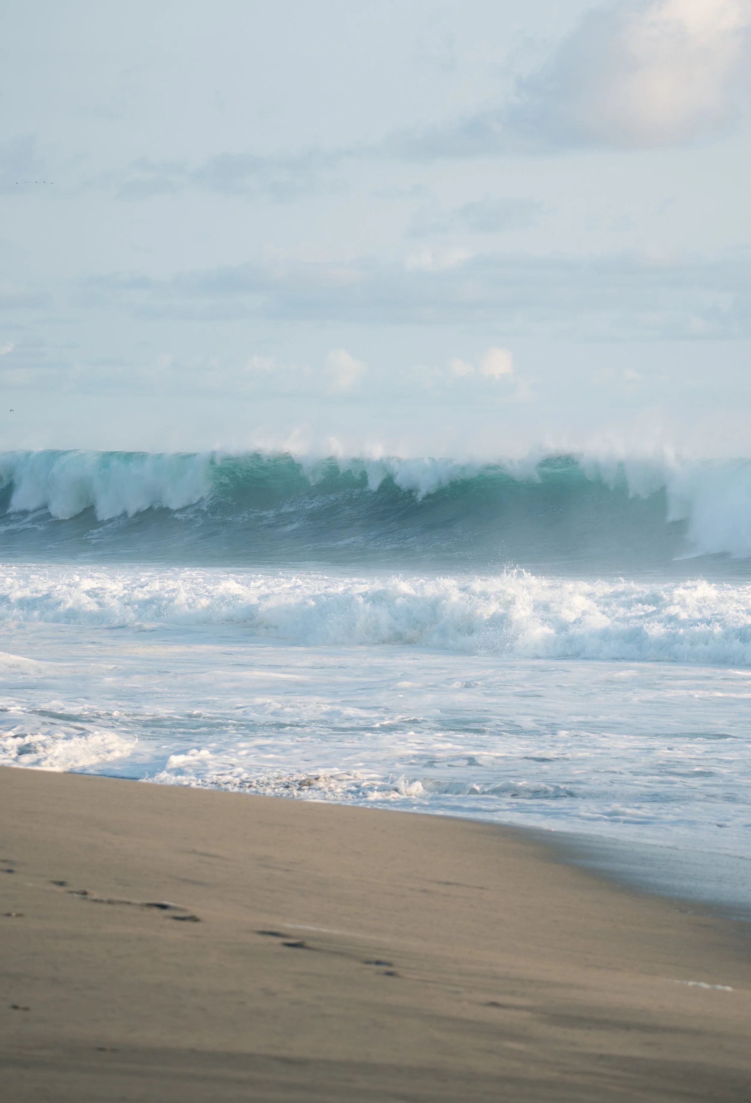 Editorial landscape photography of Atlantic Ocean waves crashing onto a sandy beach under cloudy skies