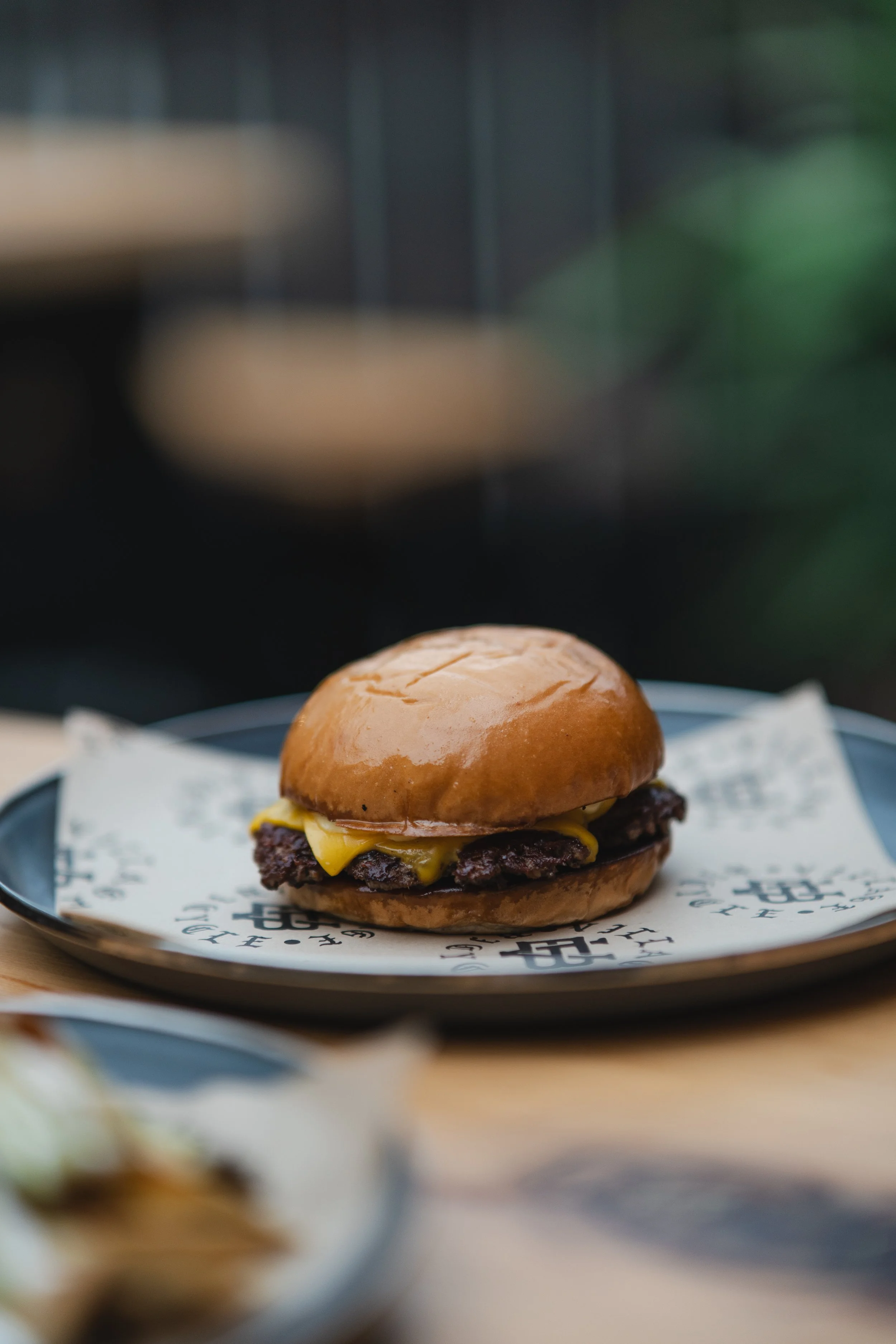 A cheeseburger with beef patty and melted cheese on a bun, served on a plate with paper liner.
