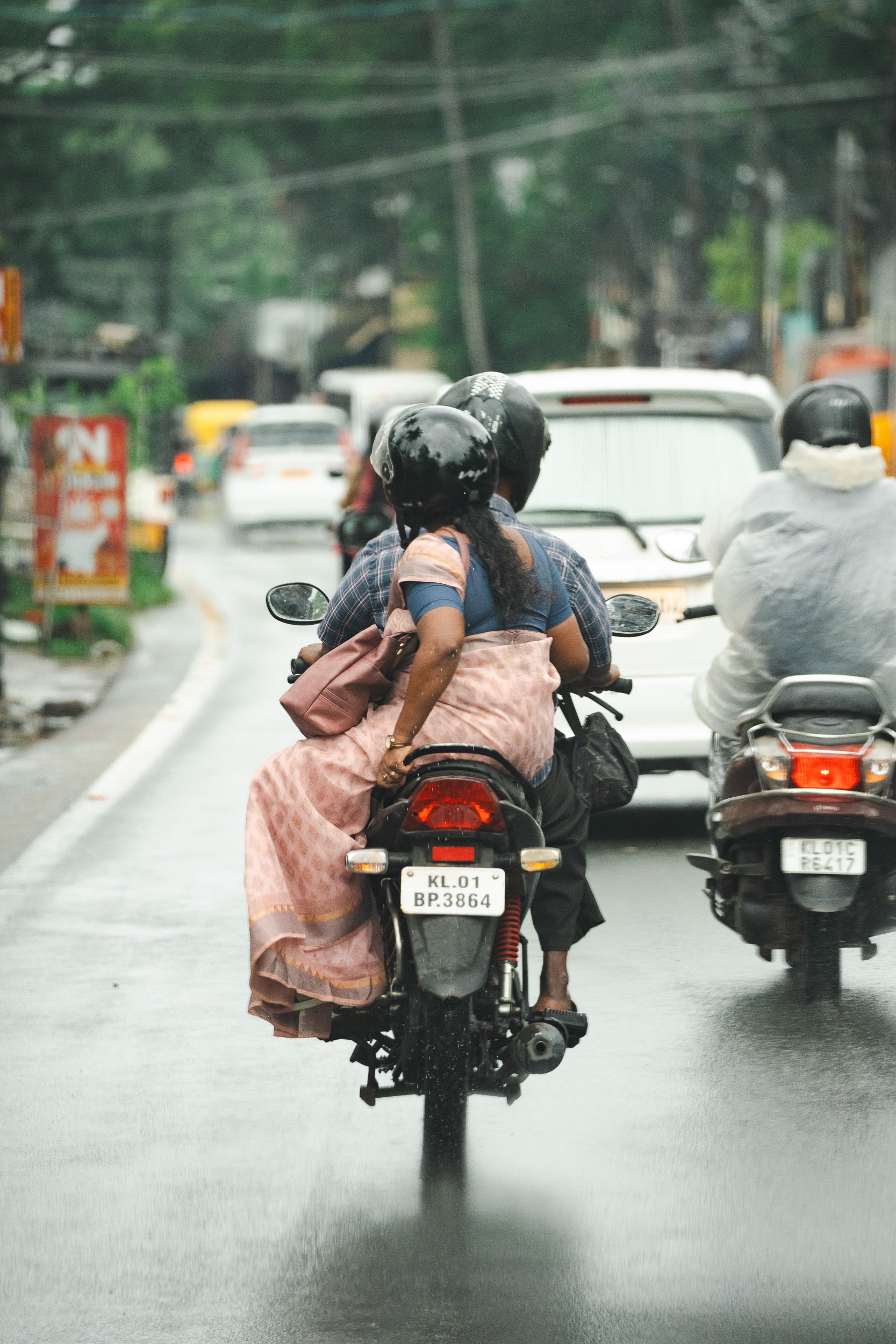 Editorial street photography in India of motorcyclists riding through a rain-soaked urban street