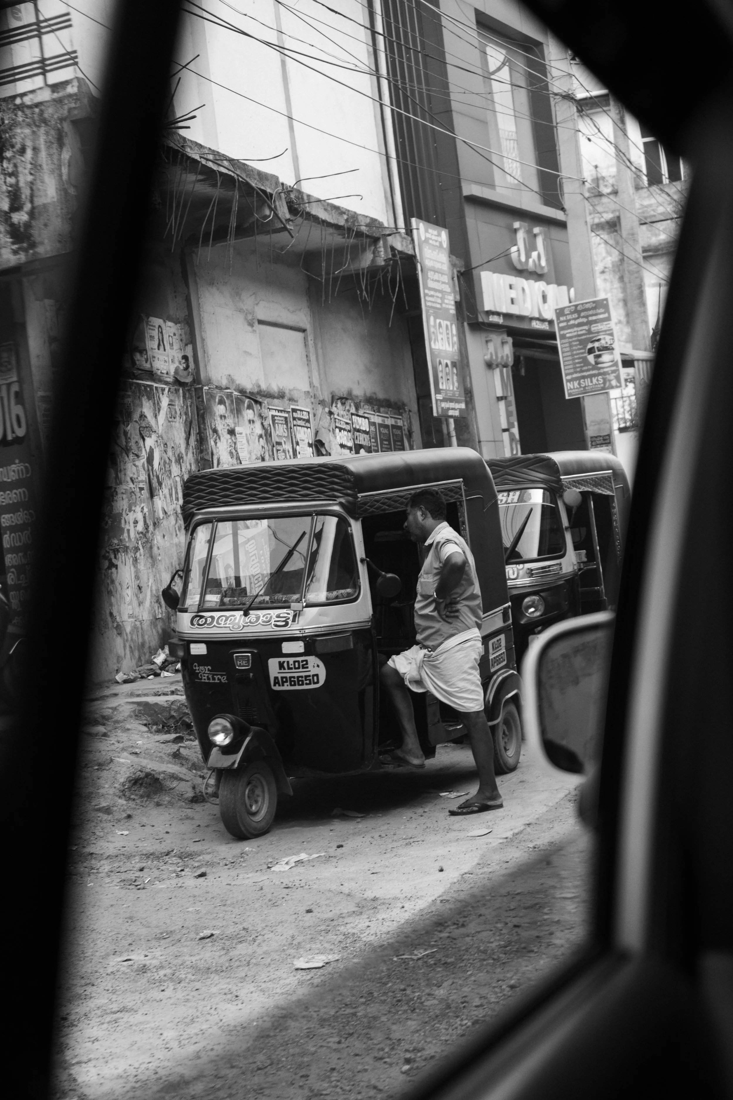 Cinematic street photography in India of a man beside an auto rickshaw seen through a vehicle window