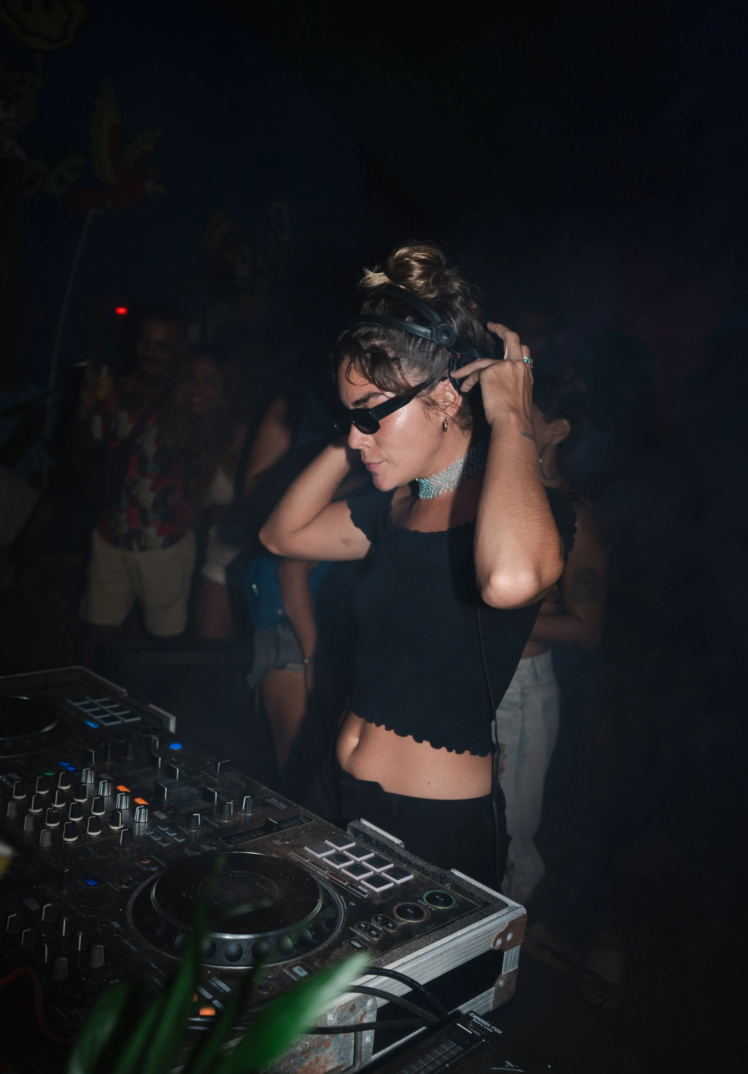 Woman DJ mixing music at a nightclub with professional DJ equipment and dancing crowd behind, dynamic event and nightlife photography