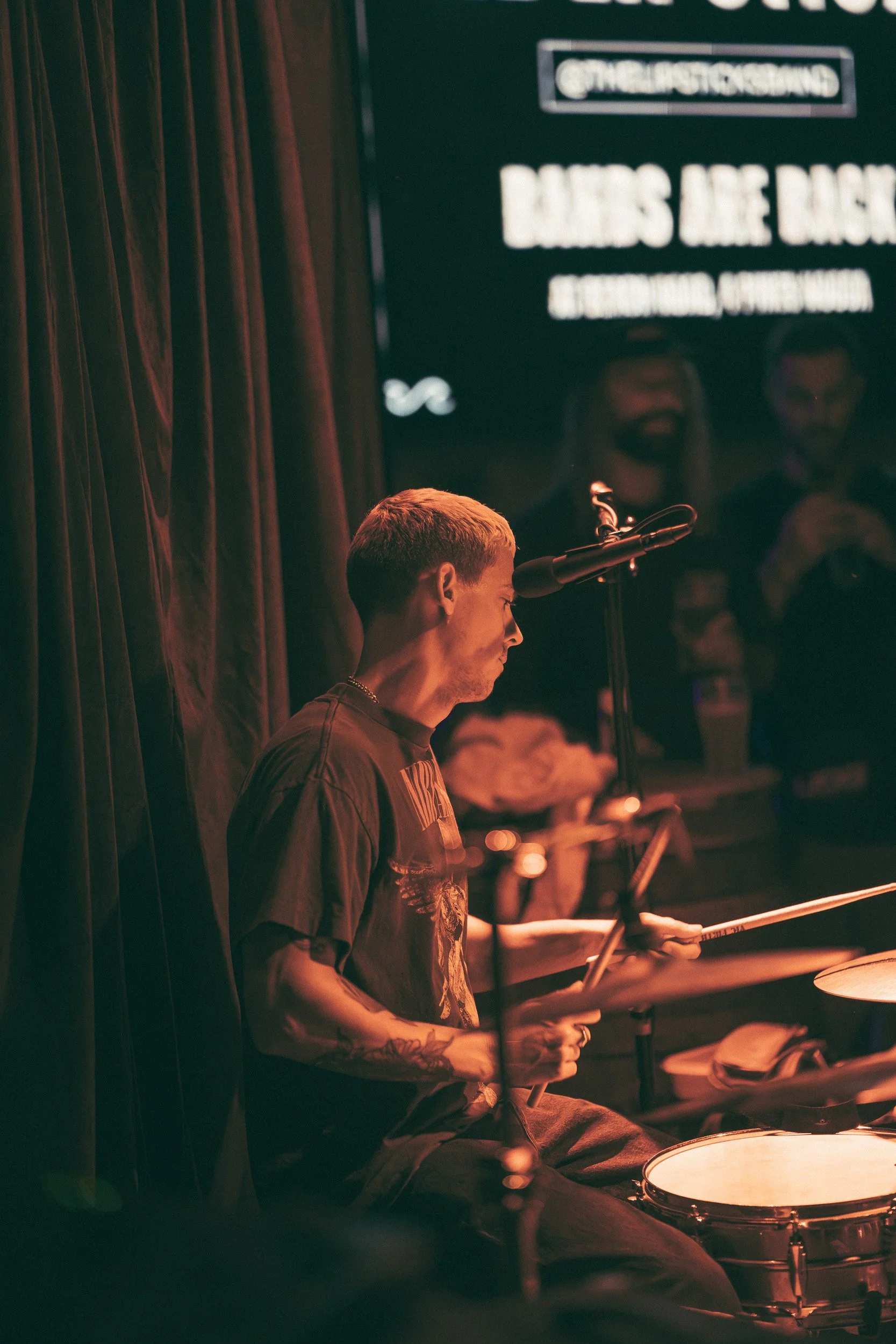 Young drummer playing live on stage in Noosa with audience in background, Sunshine Coast event and music photography