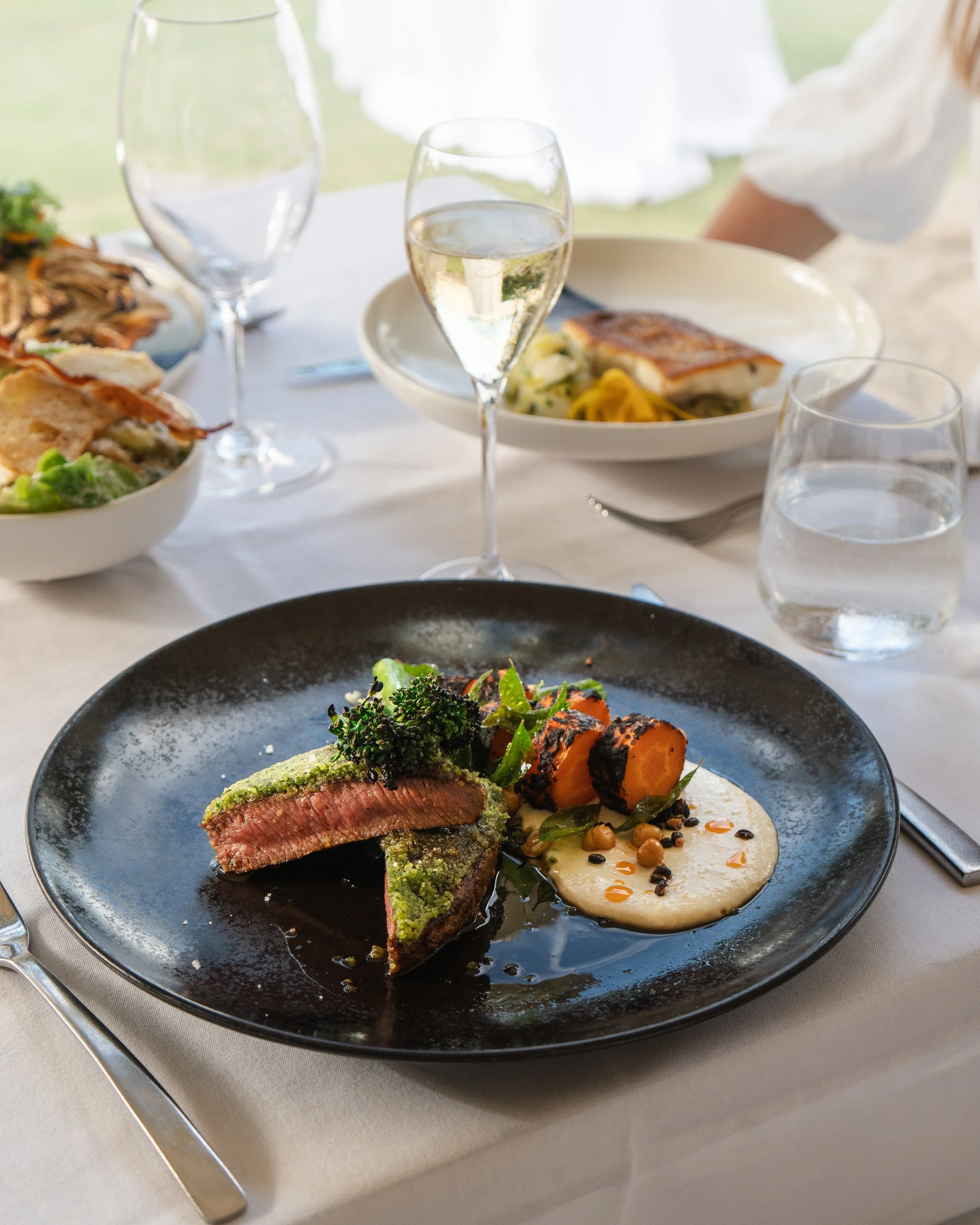 Elegant dining table with plated gourmet food, glasses of white wine, and bowls of salads.