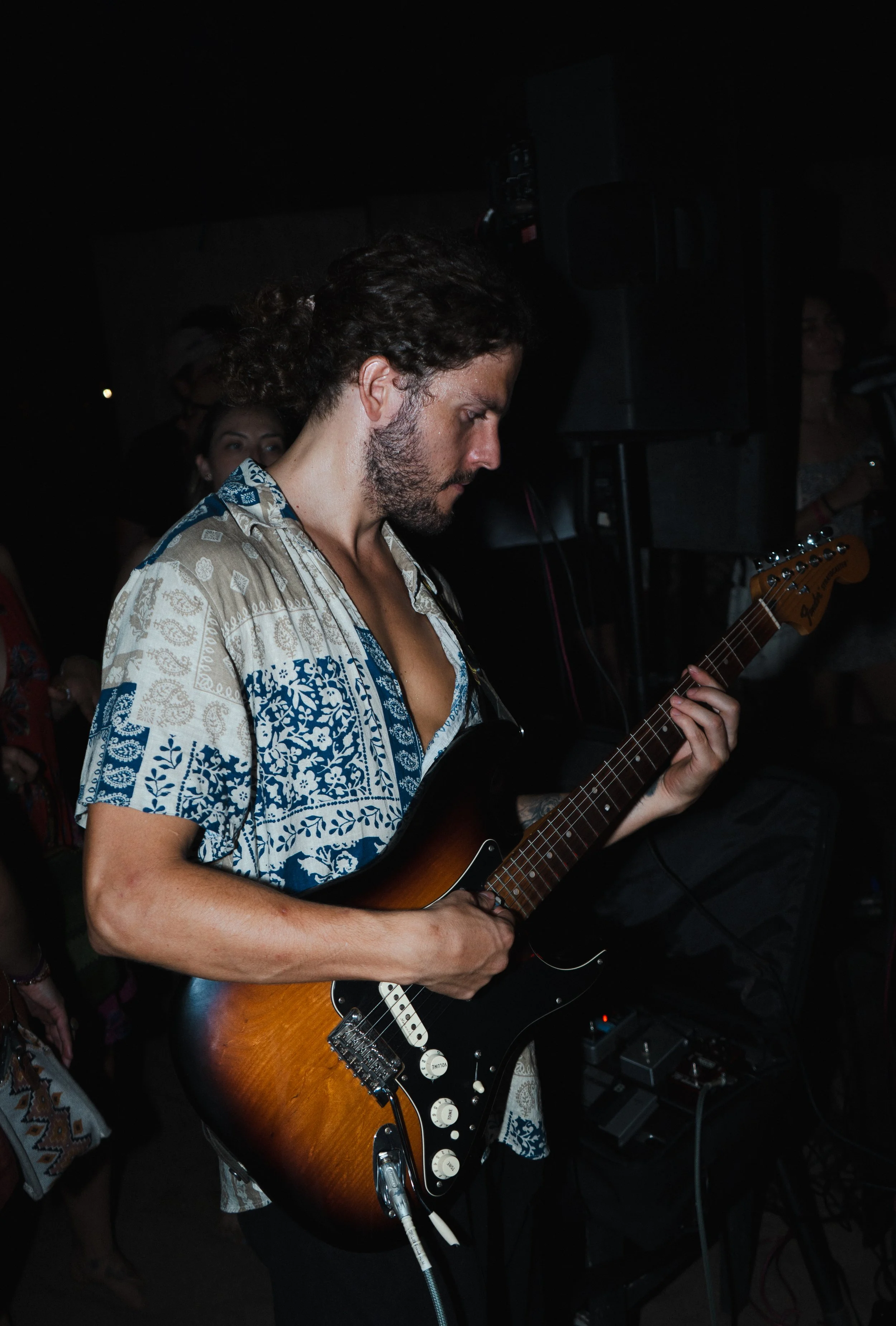 Male musician with curly hair and beard playing electric guitar at a dimly lit indoor event in Noosa, Sunshine Coast event and music photography