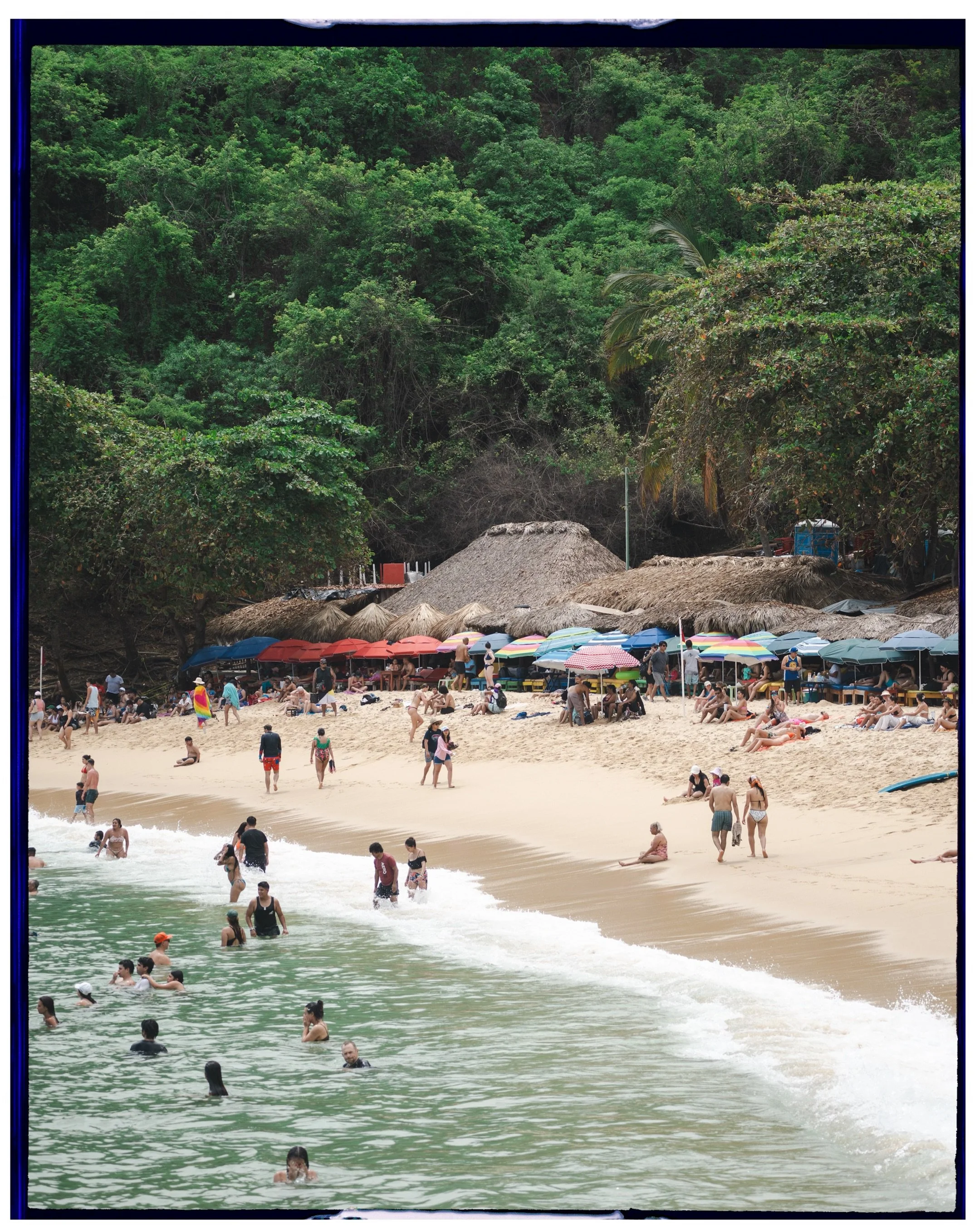 Editorial destination photography of people relaxing on a tropical beach with umbrellas and lush green backdrop