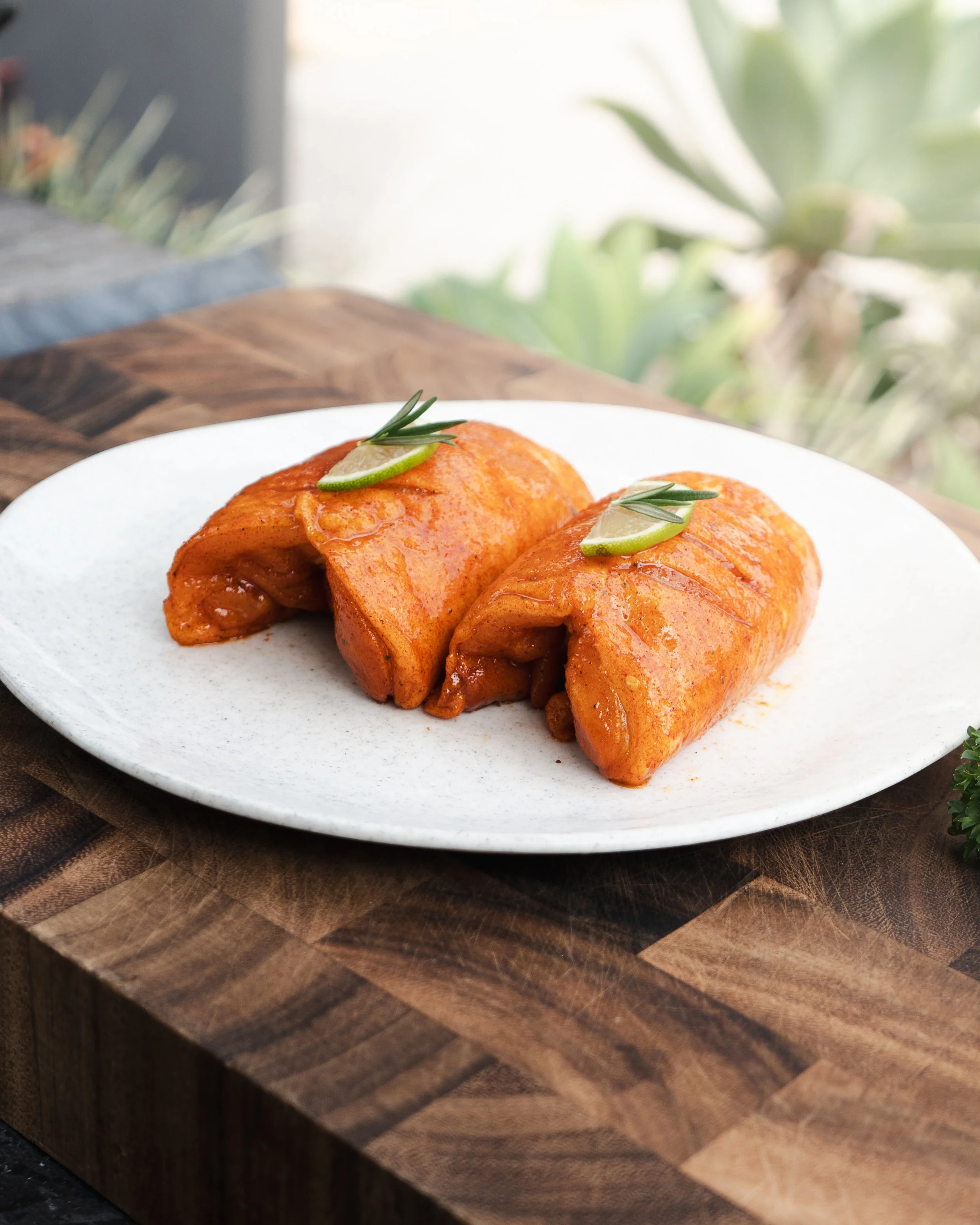 Two rolled, sauced enchiladas garnished with lime wedges and rosemary on a white plate.