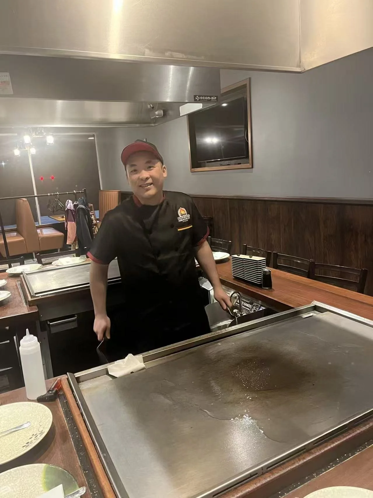 A smiling chef standing behind a teppanyaki grill.