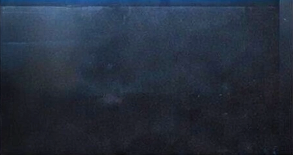 Dark, textured surface with faint reflections and spots