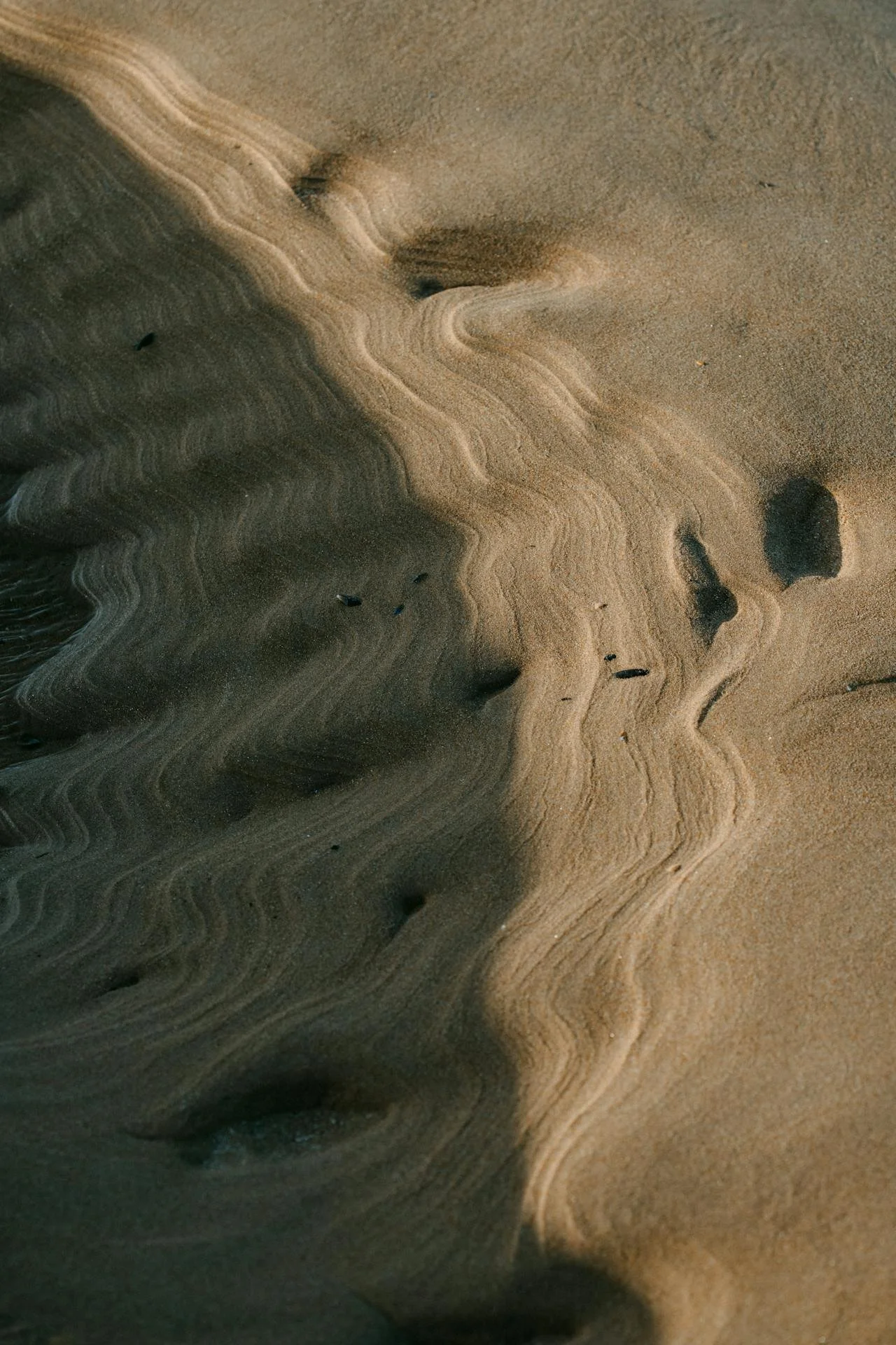 Close-up of sandy beach with layered, swirling patterns and small scattered rocks.