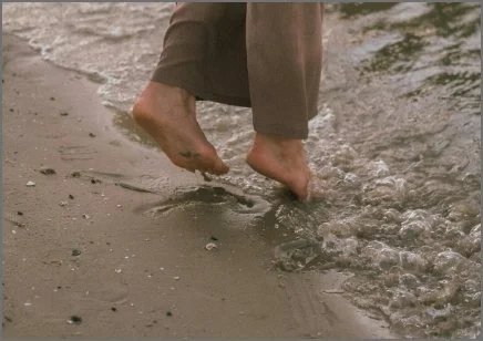 Person walking barefoot in shallow water on a sandy beach