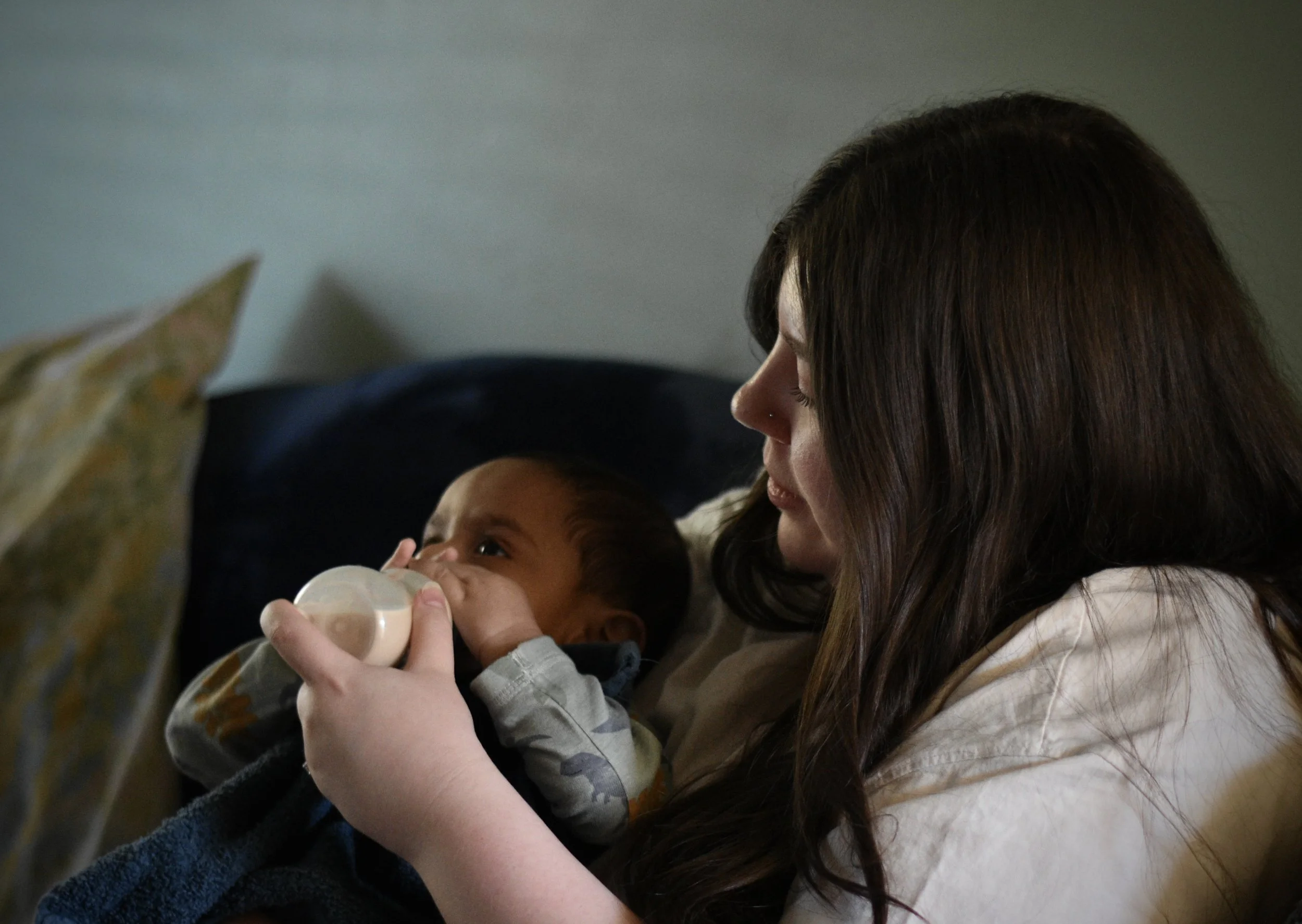 A woman with long brown hair feeding a young child with a bottle.