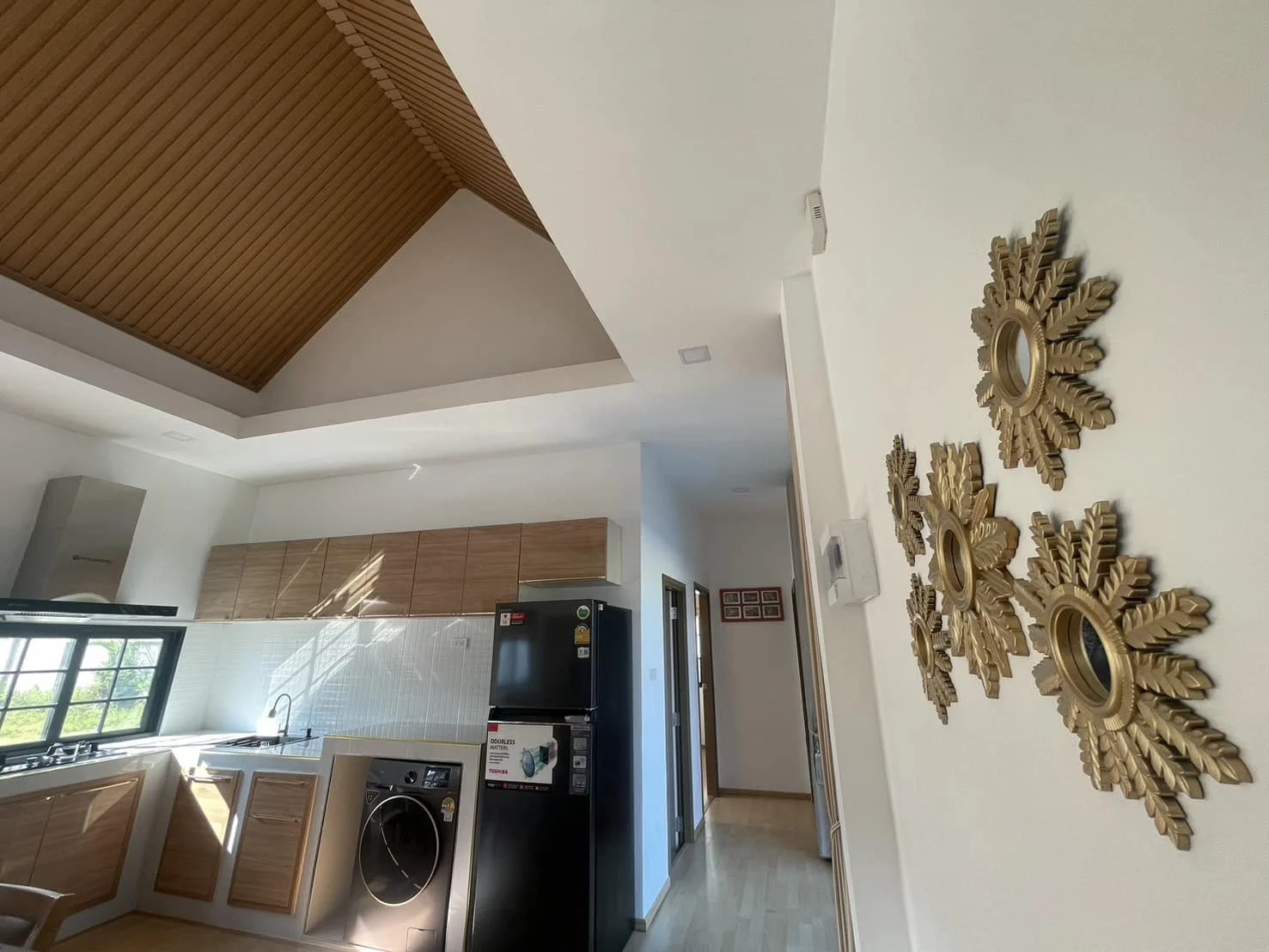 A detailed view of the interior corridor and kitchen area, featuring decorative sunburst wall art and a glimpse of the vaulted wood ceiling.