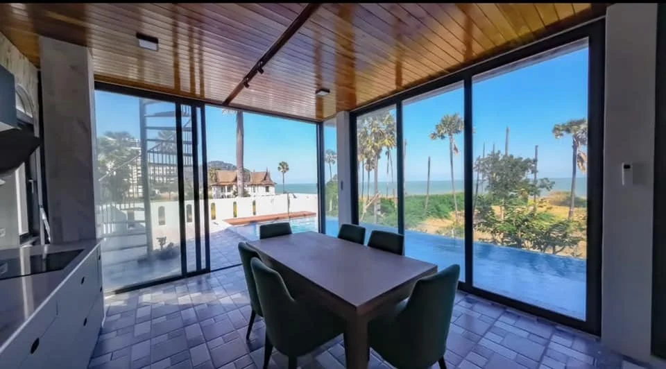 Coastal Dining: A sophisticated dining space anchored by a minimalist wooden table and deep forest-green velvet chairs.