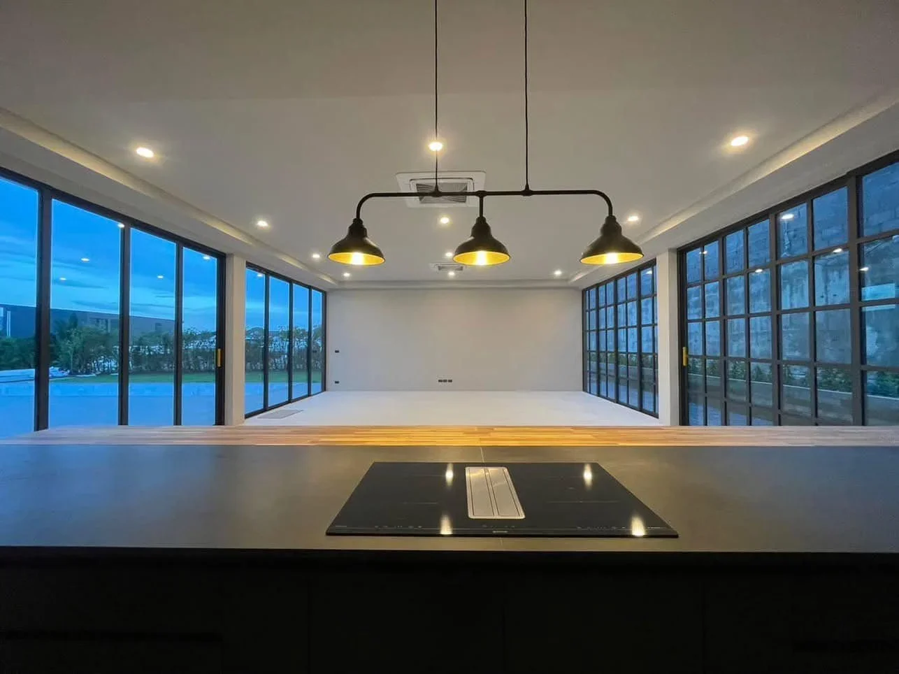 POV from the kitchen island showing the expansive open living area surrounded by floor-to-ceiling windows with mountain views.