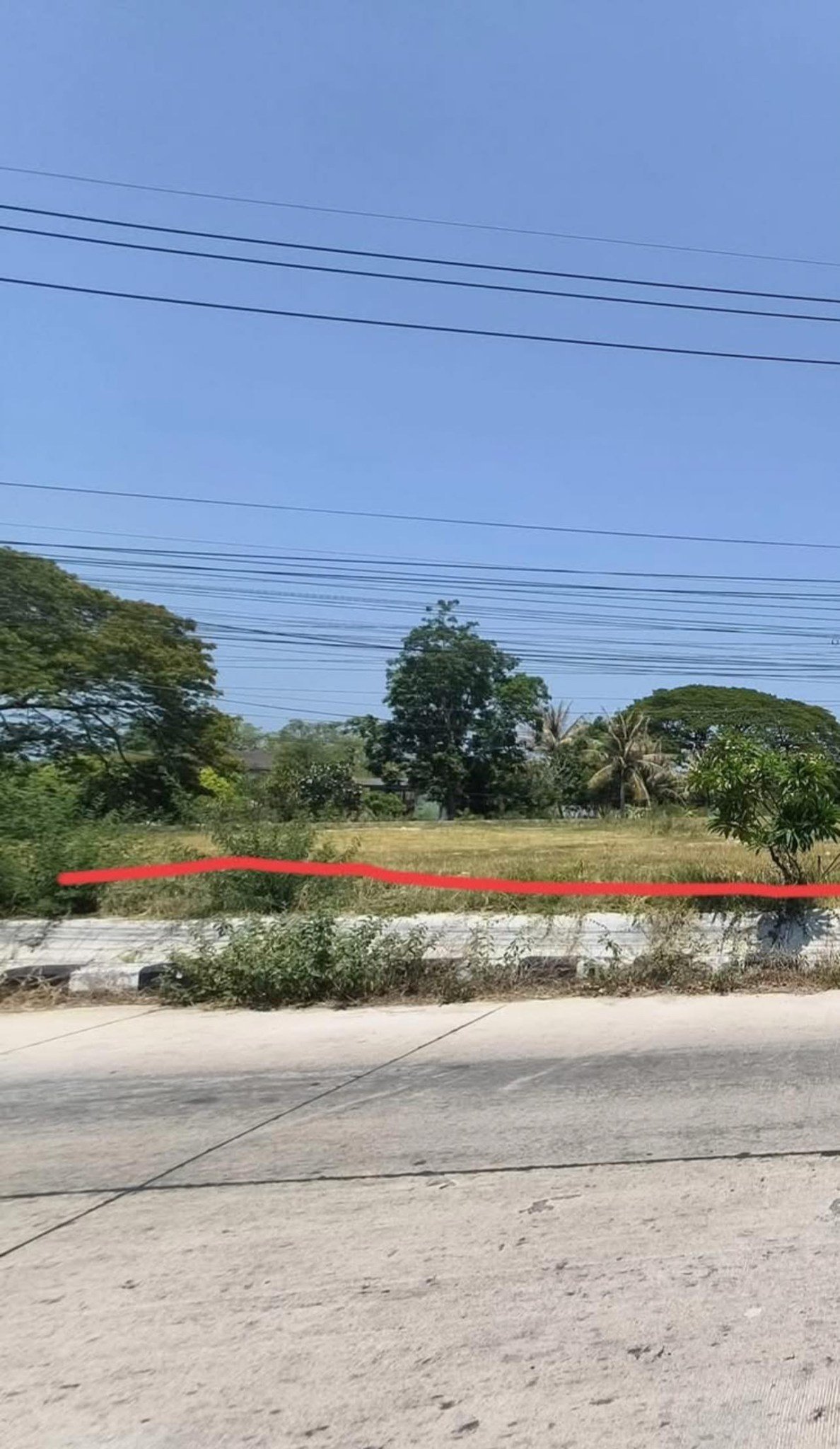 A wide-angle view from the paved access road illustrating the plot's significant street frontage and its proximity to local infrastructure.