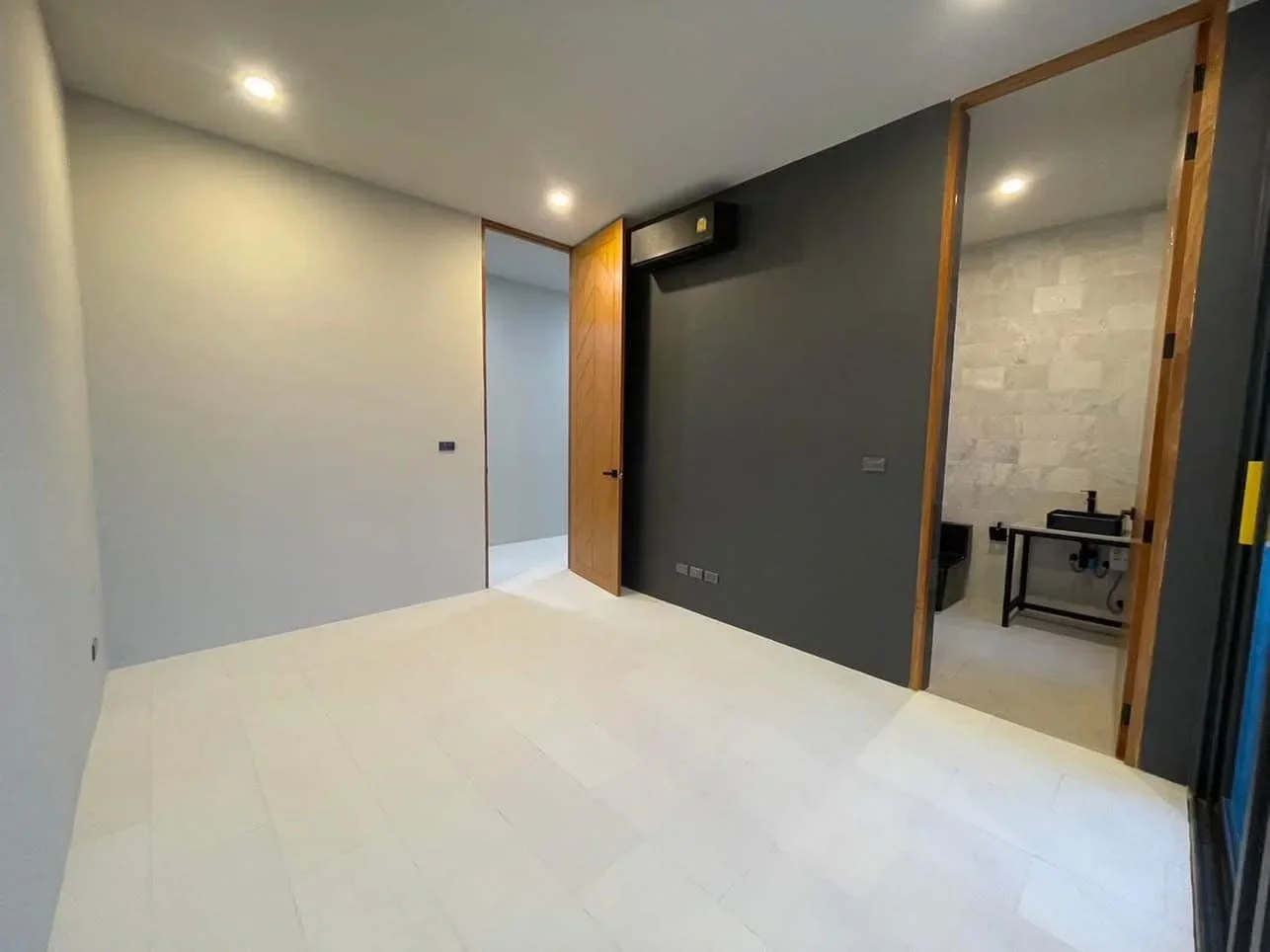 Second perspective of a guest bedroom with a dark accent wall, recessed lighting, and ensuite bathroom access in a brand-new villa.
