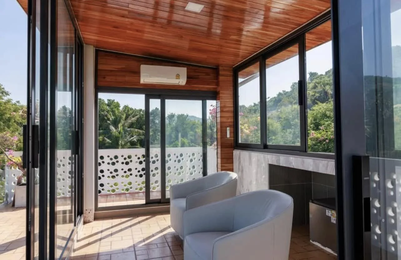 Upper Sunroom: A tranquil penthouse-level lounge characterized by warm timber ceilings and panoramic glazing