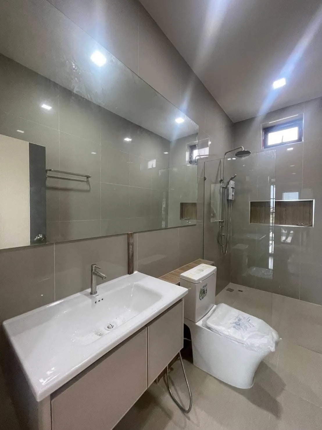 A bright and clean secondary bathroom emphasizing sleek grey wall tiling, a large vanity mirror.