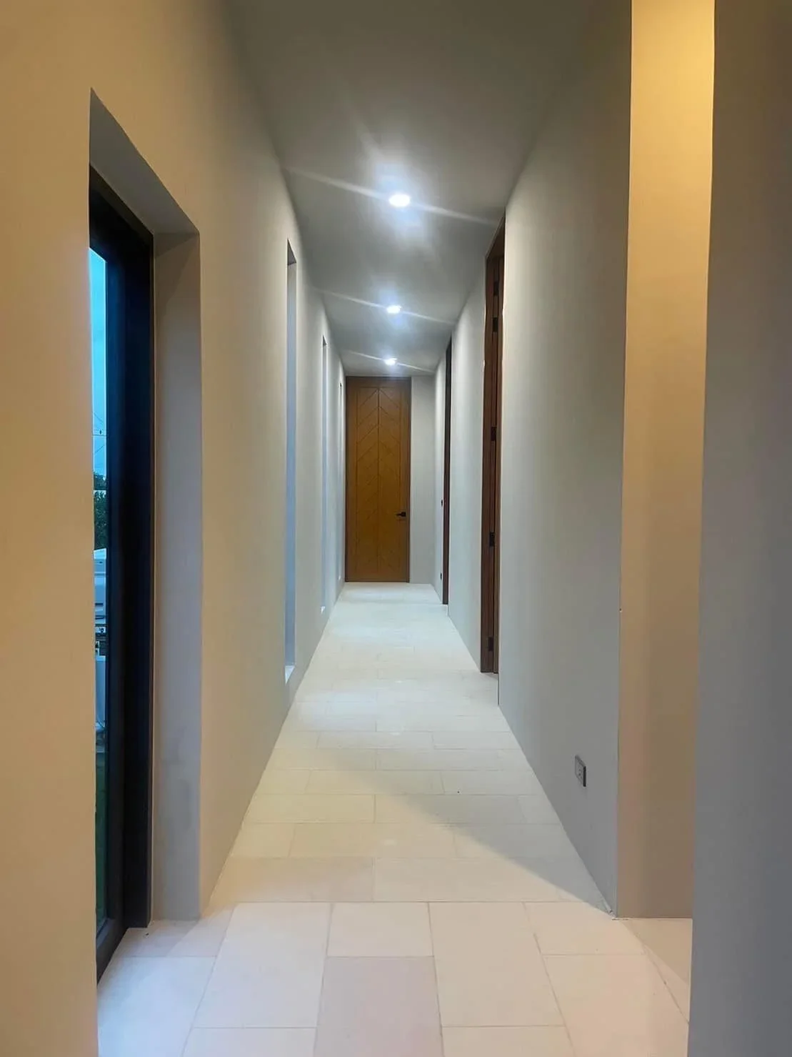 Minimalist hallway with clean white lines, natural light through narrow windows, and premium solid wood doors leading to guest bedrooms.
