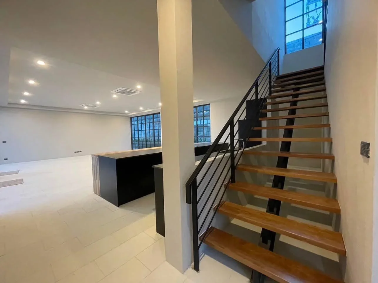 Architectural wooden staircase with black steel railings in a spacious open-plan living area of a 5-bedroom villa.