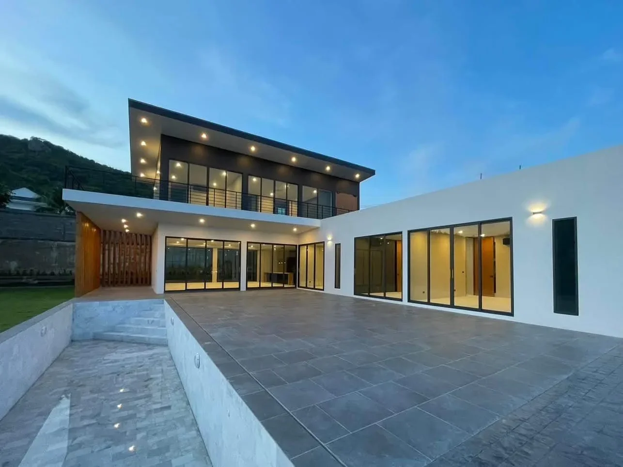 Evening exterior shot of the 5-bedroom villa with professional warm lighting, highlighting the swimming pool and indoor living spaces.