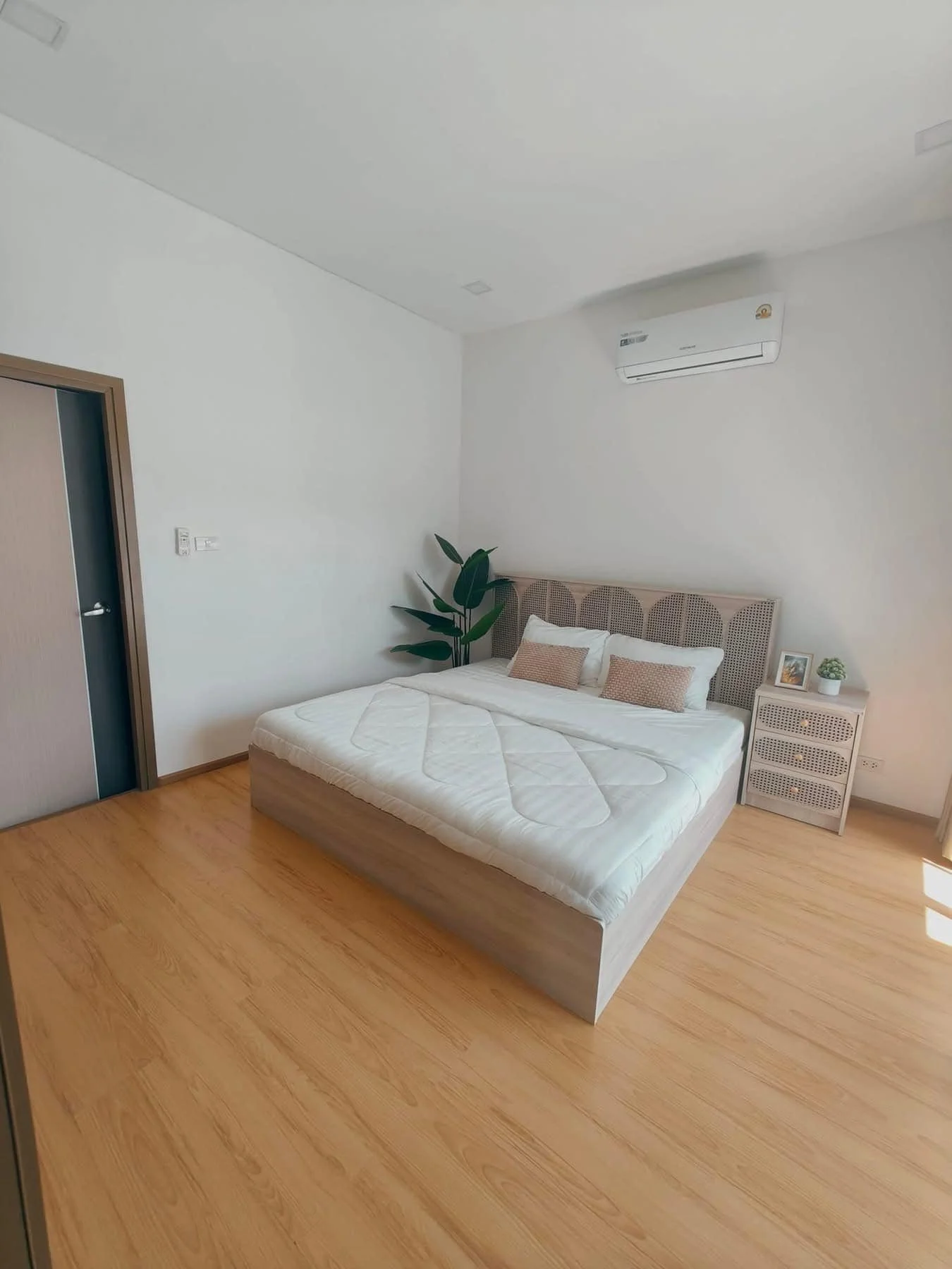 A tranquil master bedroom offering a plush queen-sized bed with a decorative woven headboard, warm wood floors.