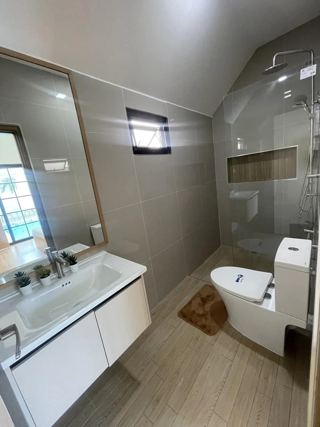 A luxury bathroom setting with neutral-toned porcelain tiling, a large vanity mirror, and a modern glass-enclosed shower area.
