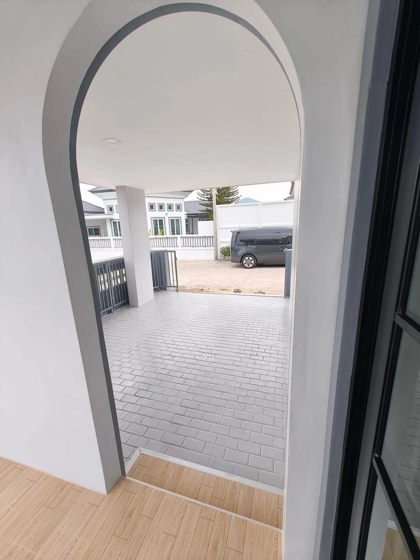 A view through a graceful arched doorway leading to a private, shaded carport with grey brick paving.