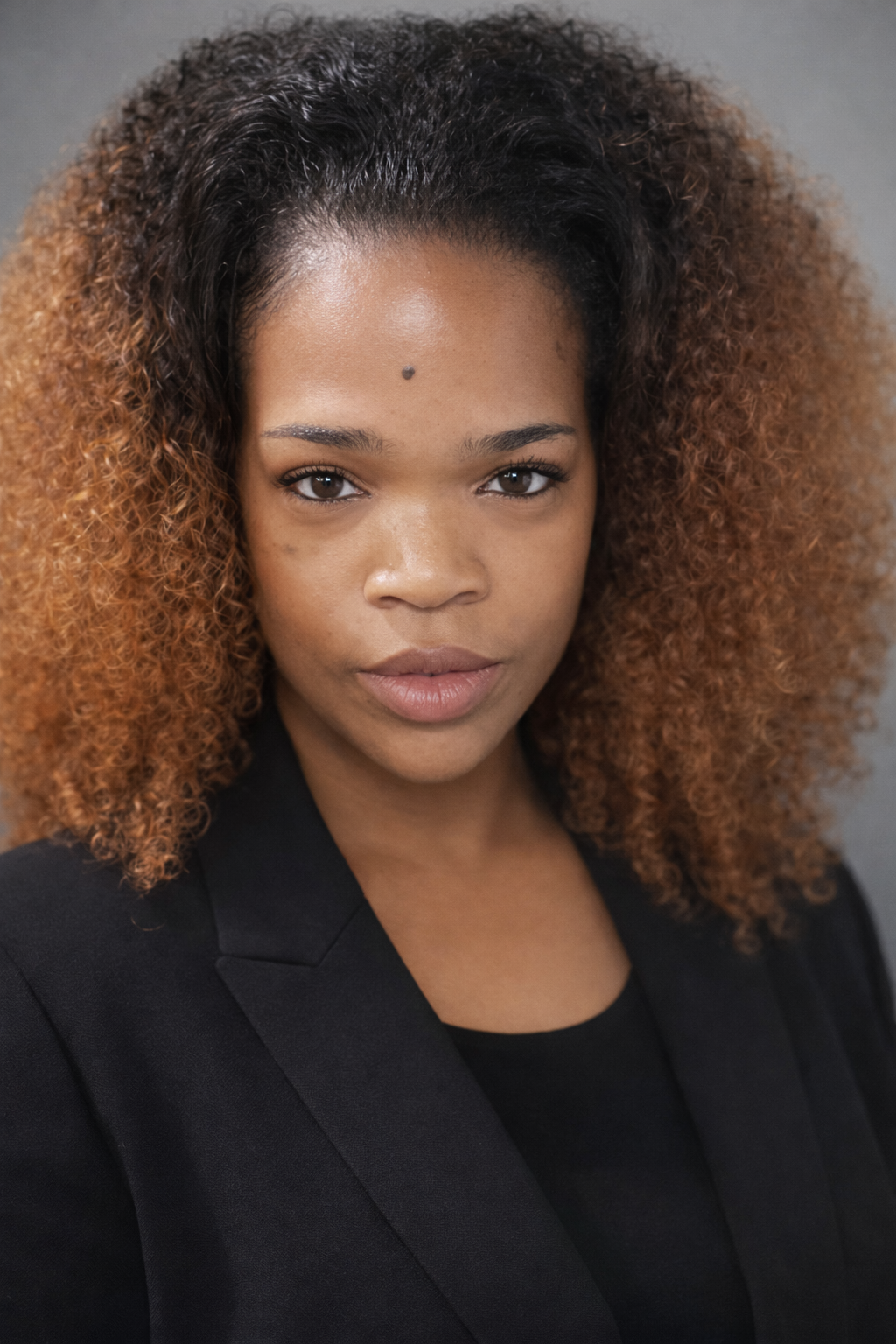 Jalisa the Author with curly hair, wearing a black blazer, looking directly at the camera with a neutral expression.