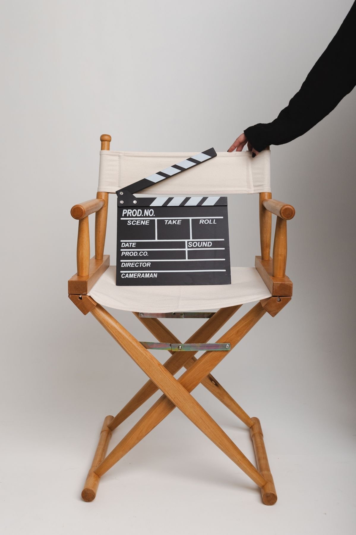 A director's chair with a black and white clapperboard placed on it, with a person's arm reaching in from the right side of the image.