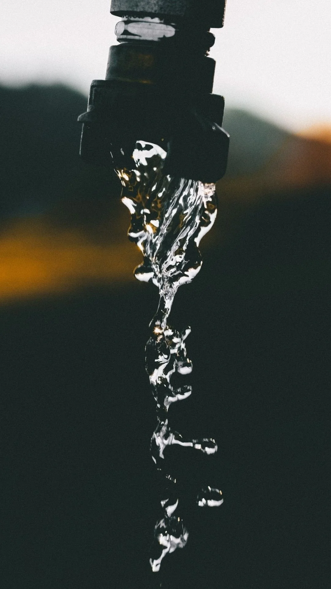 Close-up grainy image of water dripping from a hose against a dark blurred background.