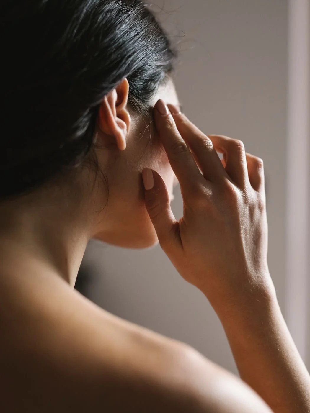 A woman with dark hair touching her face with her hand.