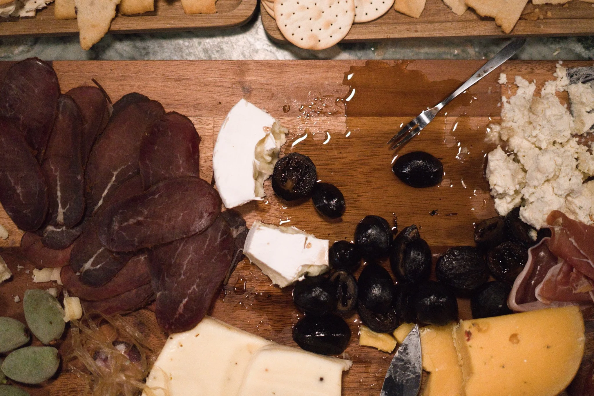 Assorted cheese, black olives, sliced cured meats, round crackers, and bread on a wooden platter.
