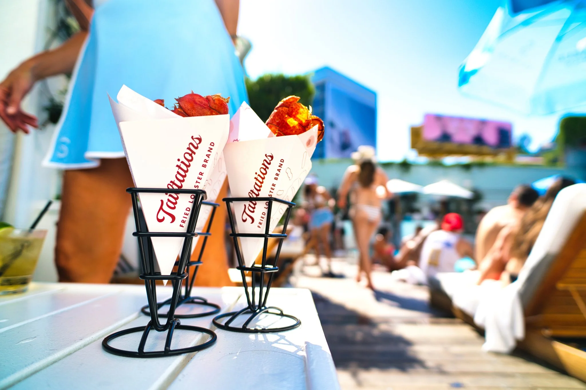 Fried Louisiana swamp catfish in takeout paper cones on a white table at an outdoor event with people in the background and a blue sky.
