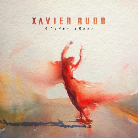 Album cover art featuring a watercolor painting of a person dancing on roller skates, with arms raised, in red hues. The text above reads "Xavier Rudd" and below "Stoney Creek."