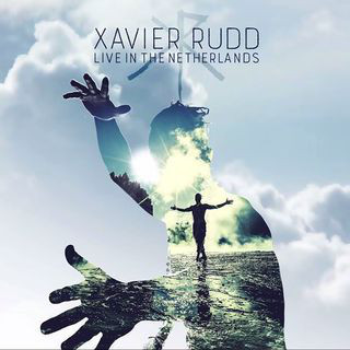 Album cover art for Xavier Rudd's "Live in the Netherlands" featuring a double exposure of a person standing in water with arms outstretched and hands reaching towards the sky, integrated with a cloud-filled sky and a hand silhouette.