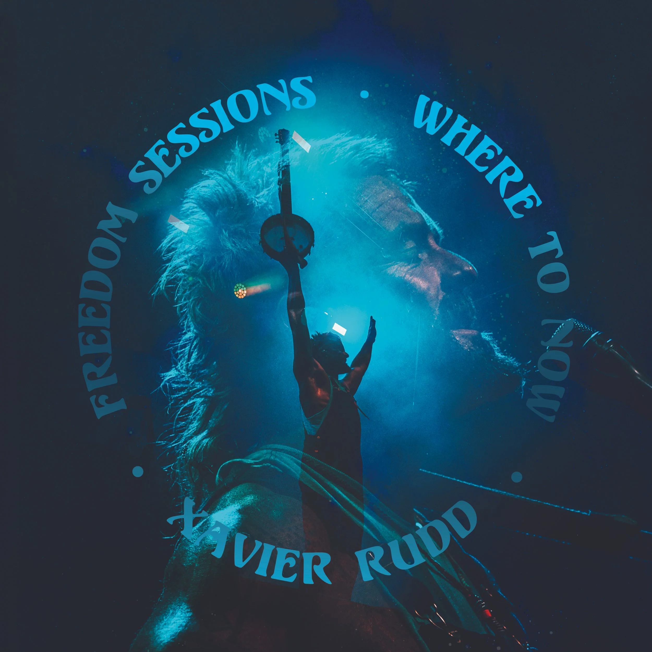 A performer on stage holding a microphone and a guitar, with a large face of a man with long hair and a beard in the background. The stage is illuminated with blue lighting, and there is text that reads 'FREEDOM SESSIONS WHERE TO NOW' and 'TAVIER RUD