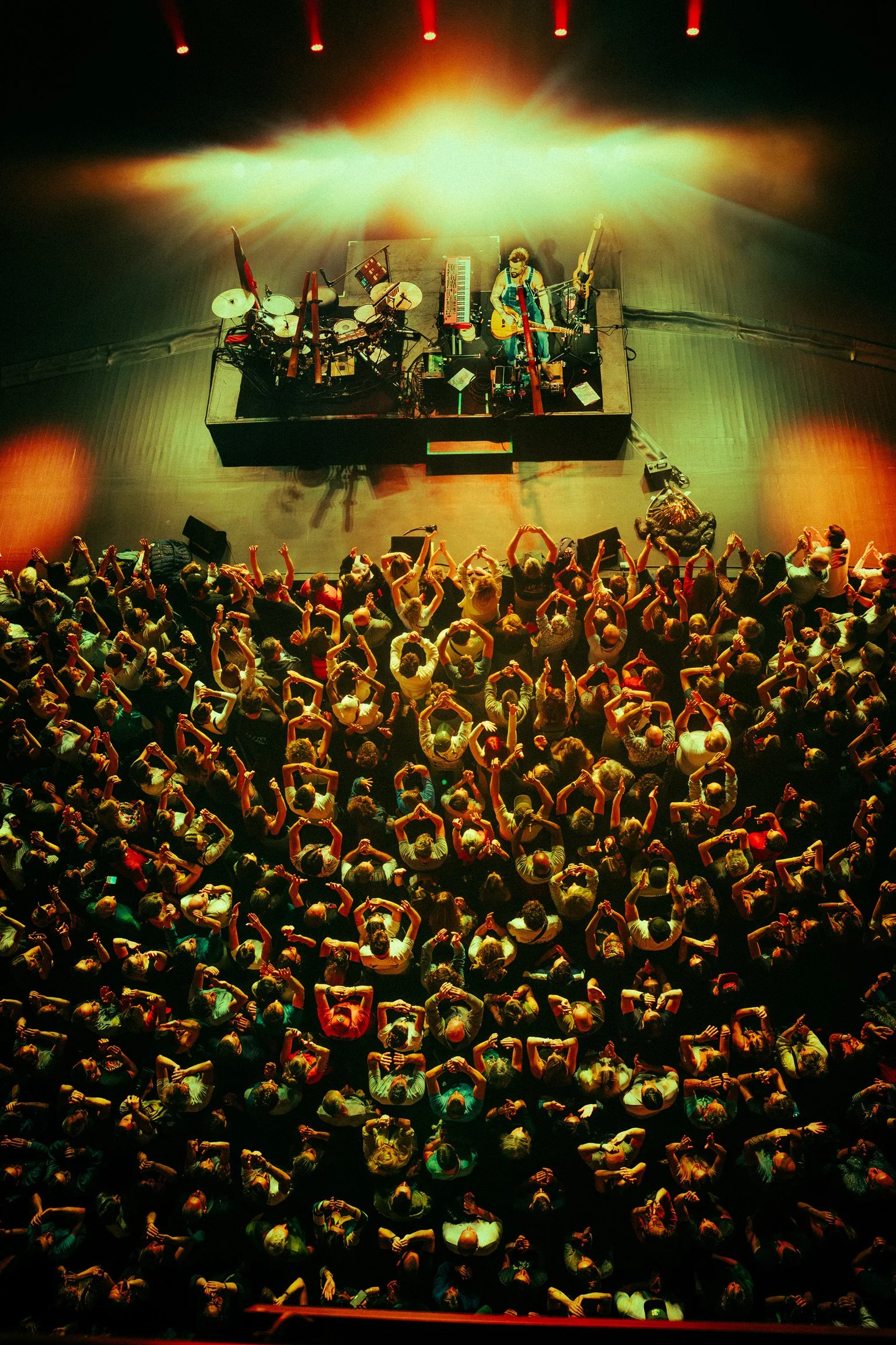 An aerial view of a live concert with a crowd dancing and a musician playing guitar on stage, surrounded by colorful stage lighting.