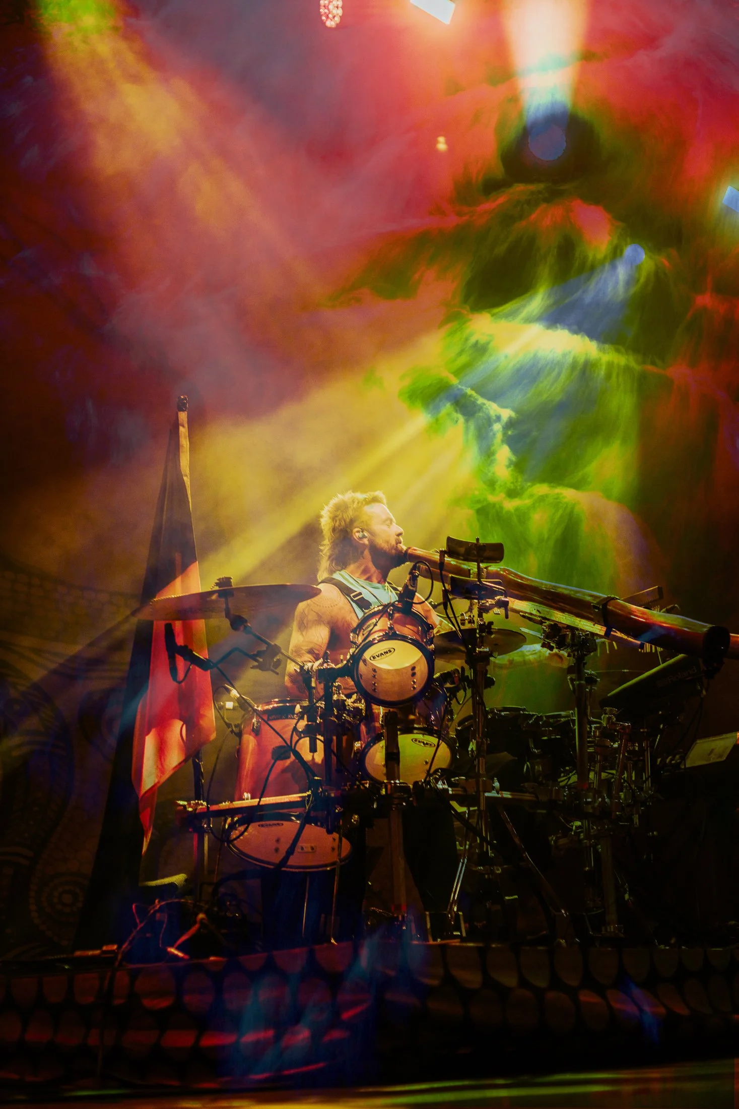 A musician playing drums on stage with colorful, vibrant lighting and smoke effects.