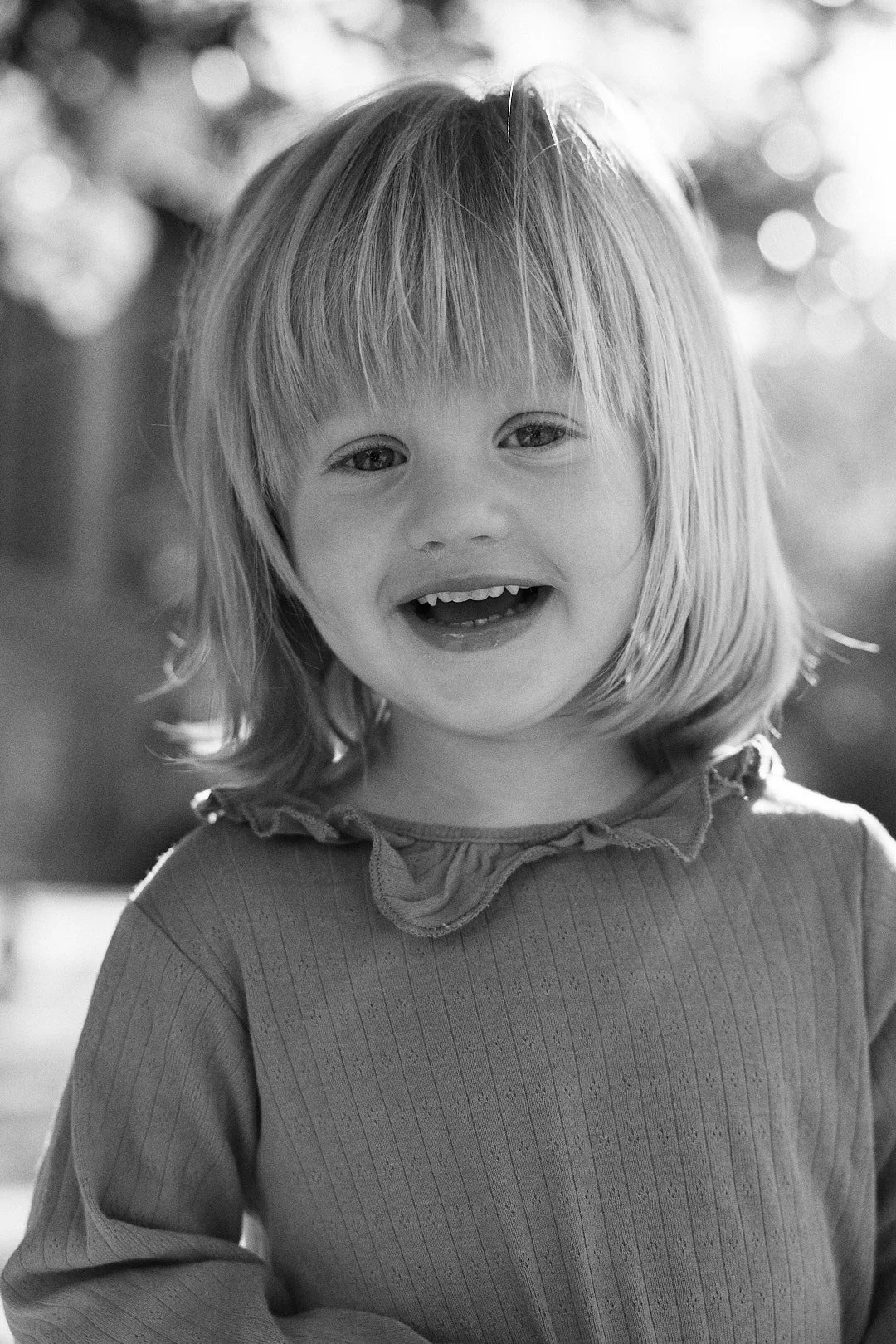 A young girl smiling outdoors on a sunny day in black and white.