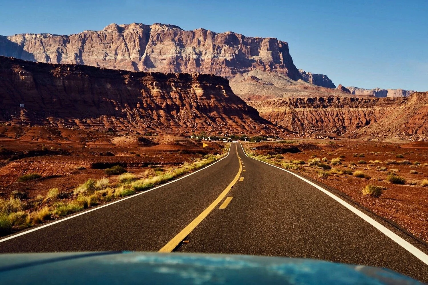 A straight road leads towards colorful desert mountains under a clear blue sky.