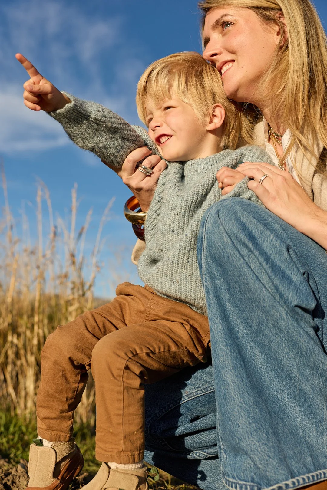 A woman and a young boy outdoors, with the woman smiling and the boy pointing at something in the distance.