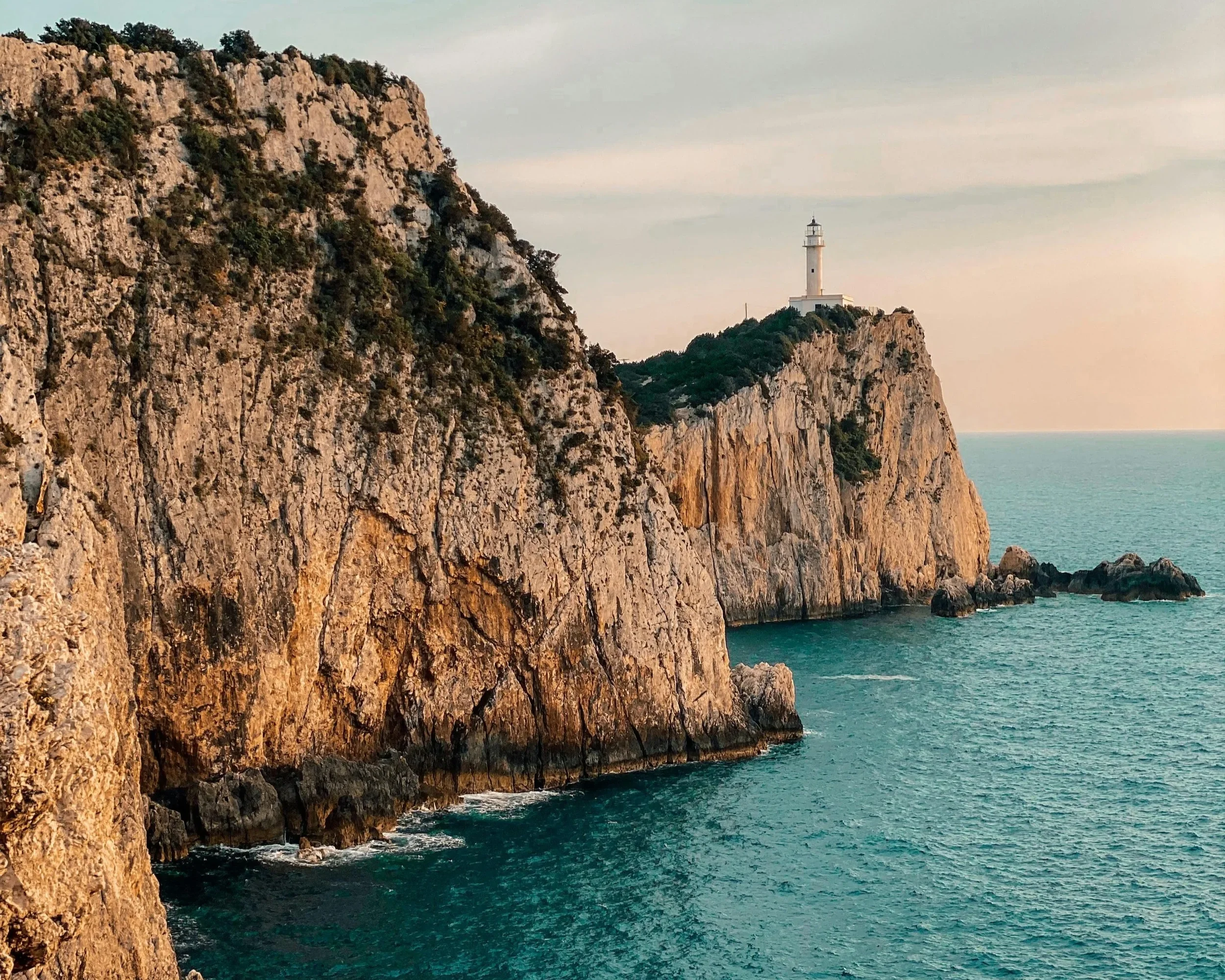 Cliffs along a rocky coastline with a lighthouse on top, overlooking the ocean during sunset.