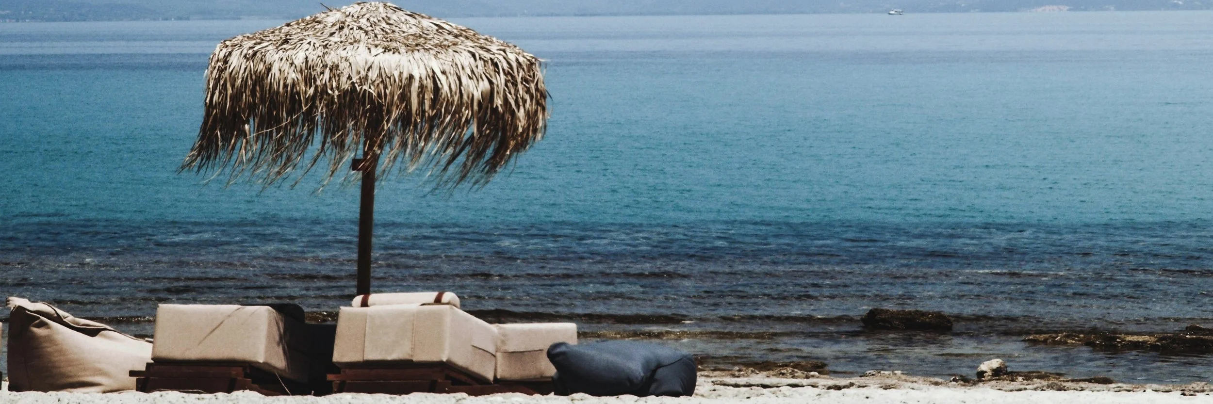 A beach scene with a thatched umbrella, lounge chairs, and a calm ocean in the background.